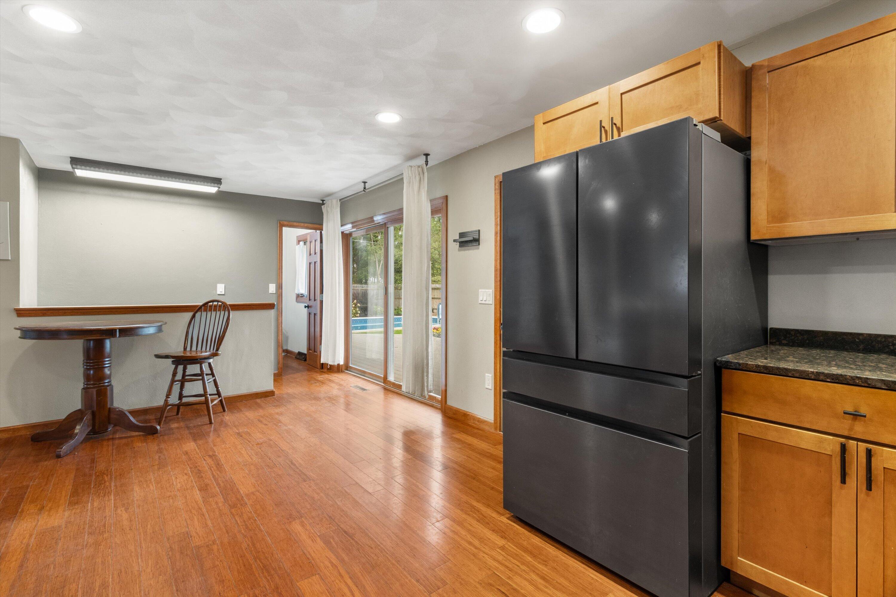 Kitchen with wood cabinets and floors, a large black refrigerator, and sliding doors overlooking a pool.