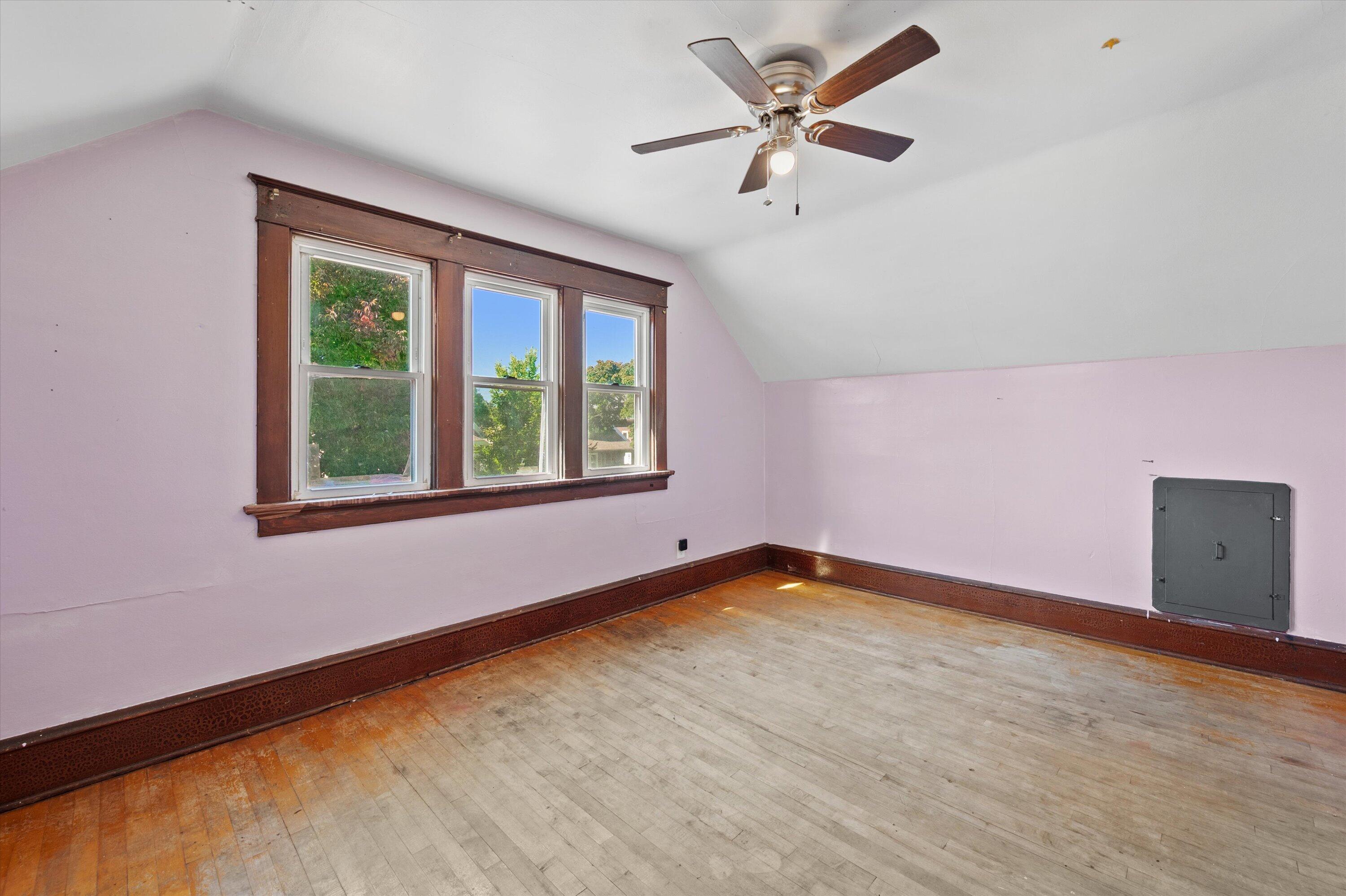 Empty room with three dark-trimmed windows, worn hardwood floors, and a ceiling fan.