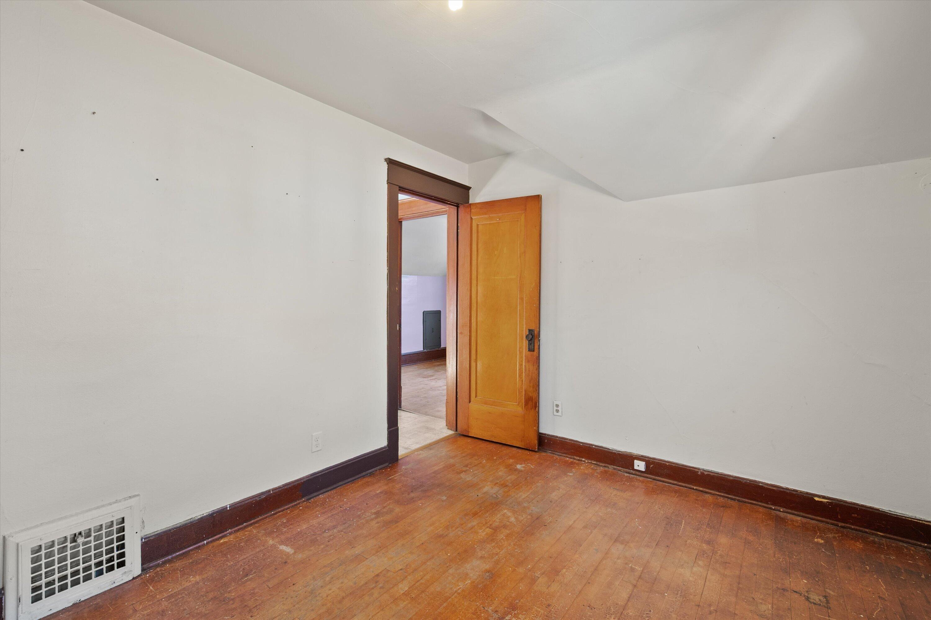 Empty room with worn hardwood floors, dark wood trim, and an open wooden door.