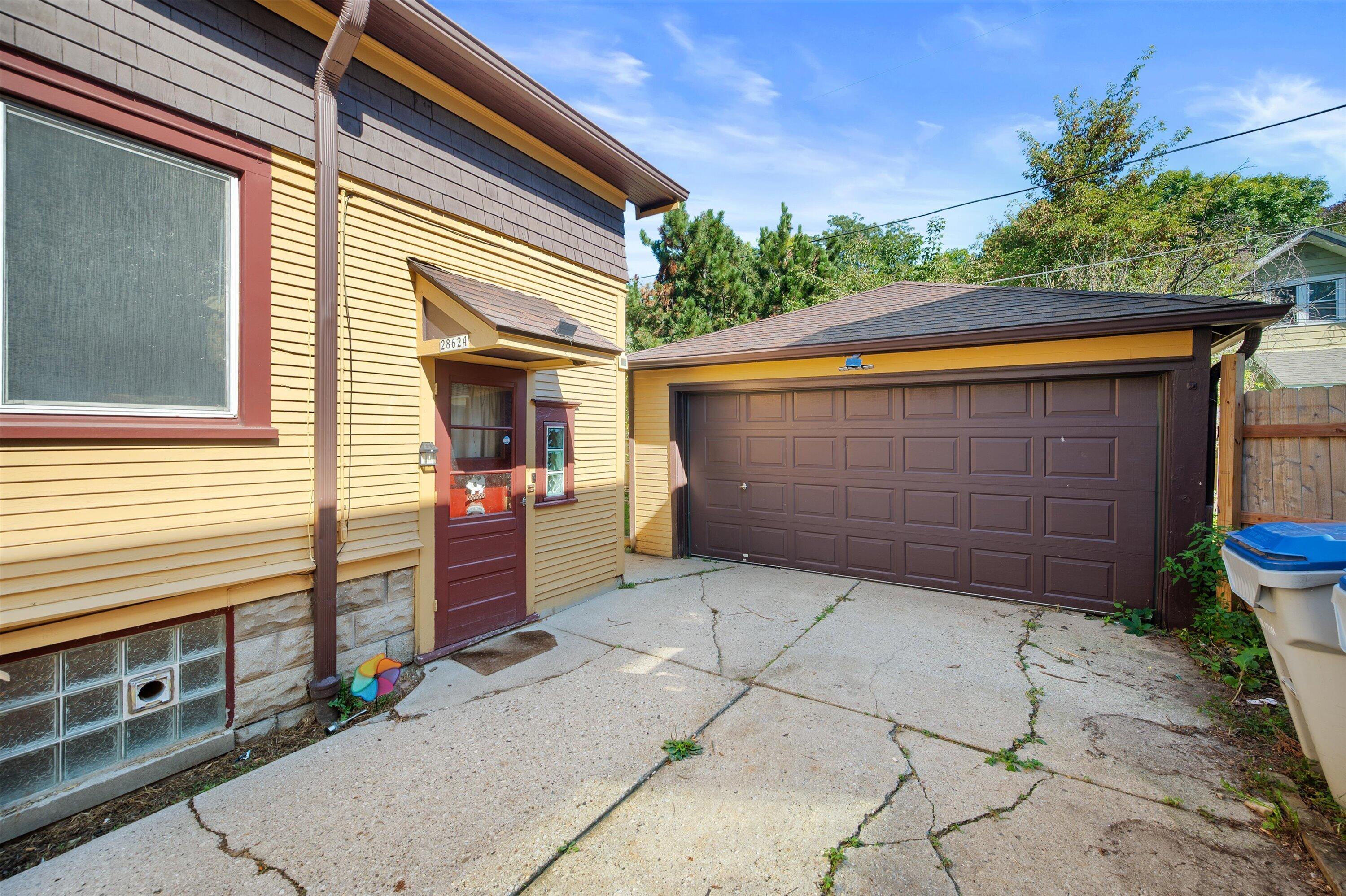 Yellow-sided house and brown garage beside a cracked concrete driveway.