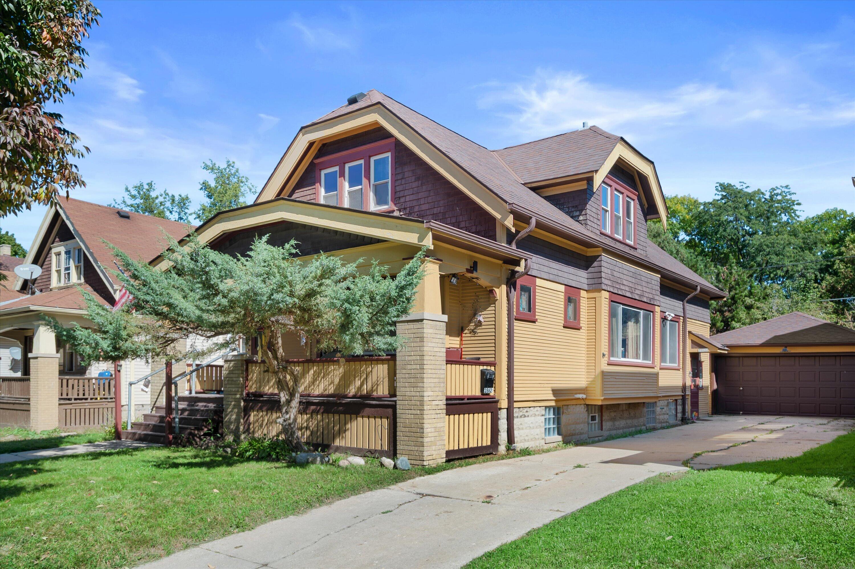 Milwaukee house with a covered porch, yellow siding, and driveway to a detached garage.