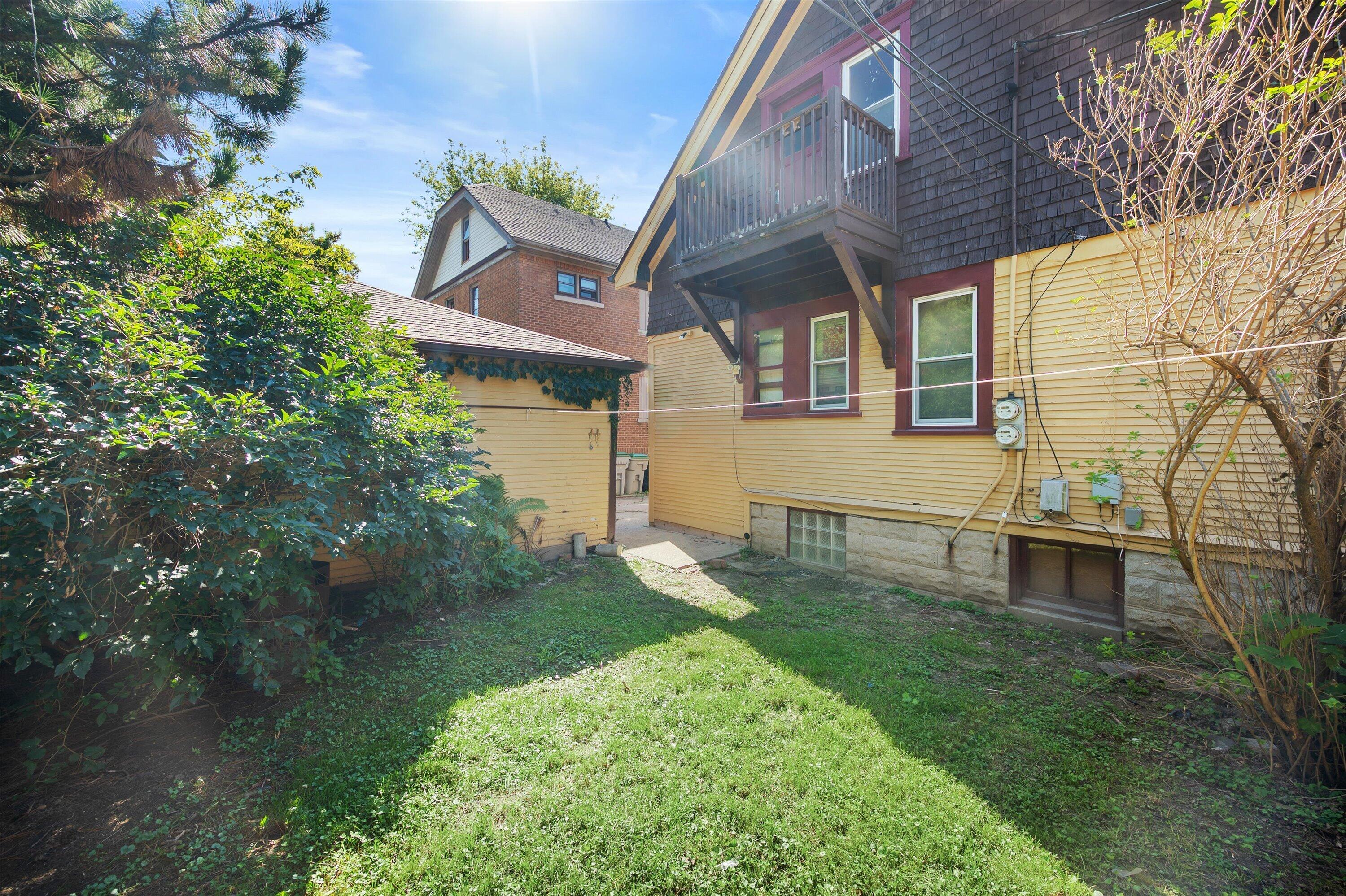 Rear of a yellow-sided house with a second-story balcony and a leafy grassy yard.