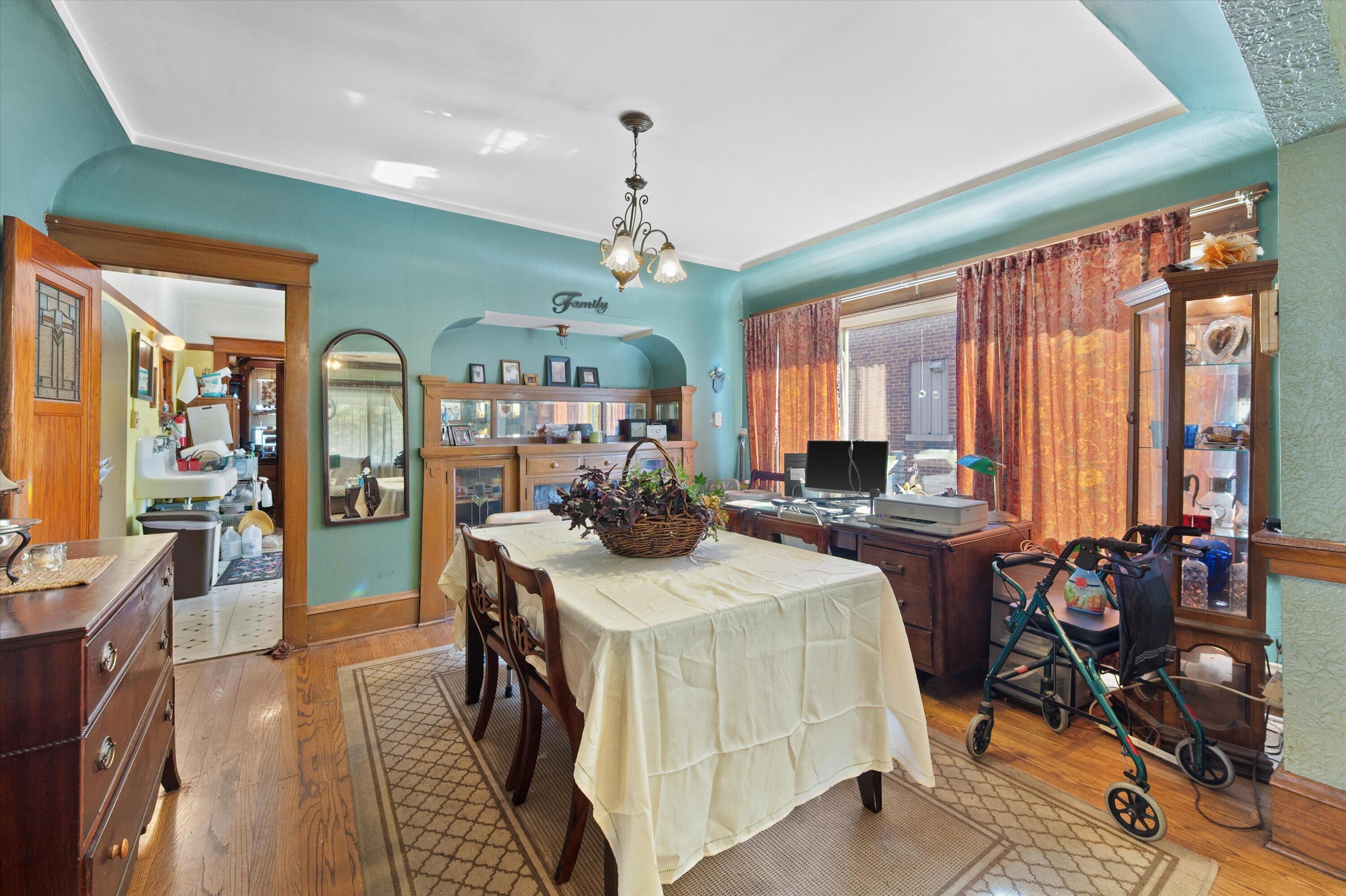 Dining room with teal walls, a white-covered table, built-in wood cabinets, and large curtained windows.