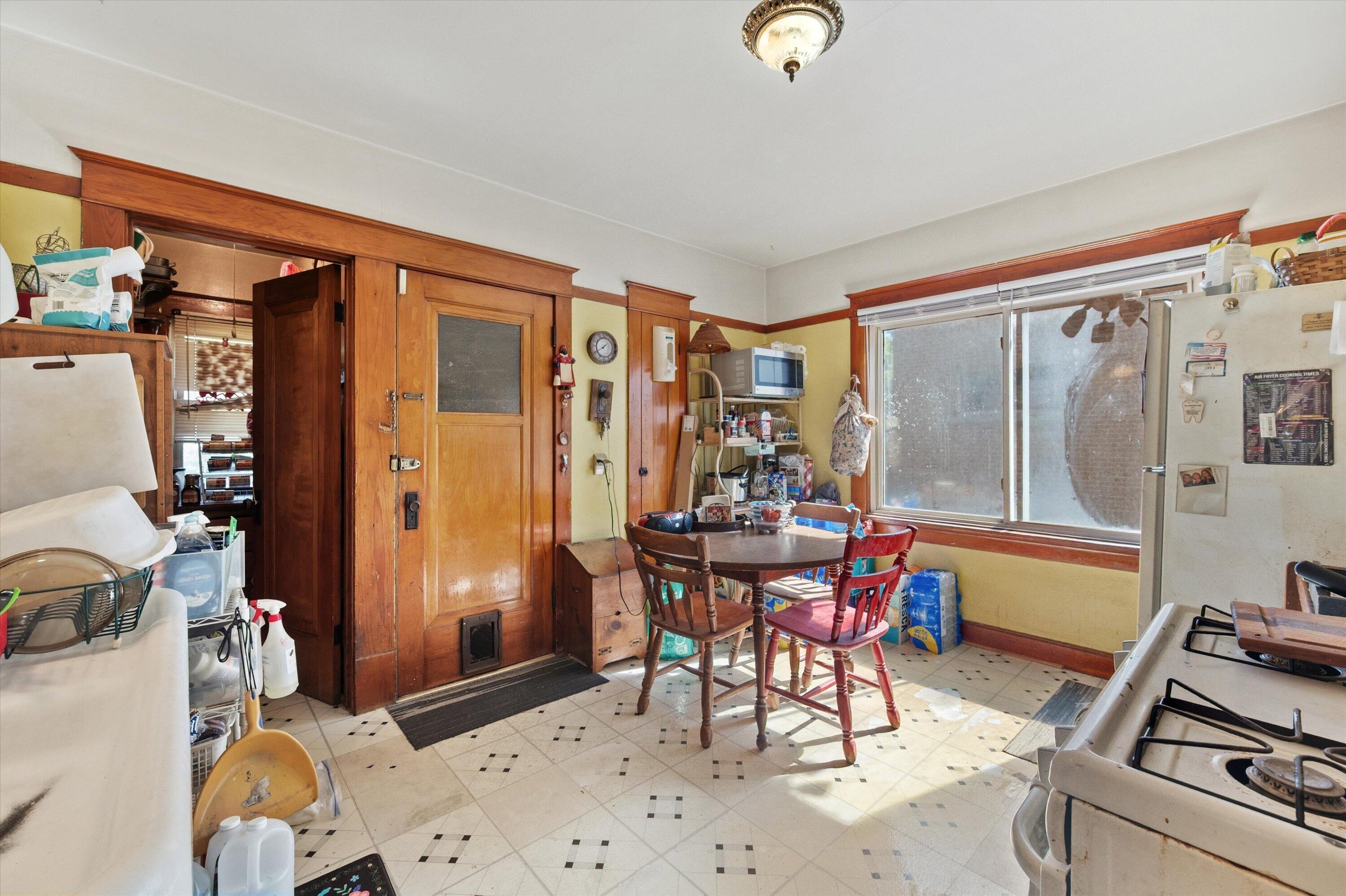 Kitchen with warm wood trim, patterned tile floor, and a small dining table beside a large window.