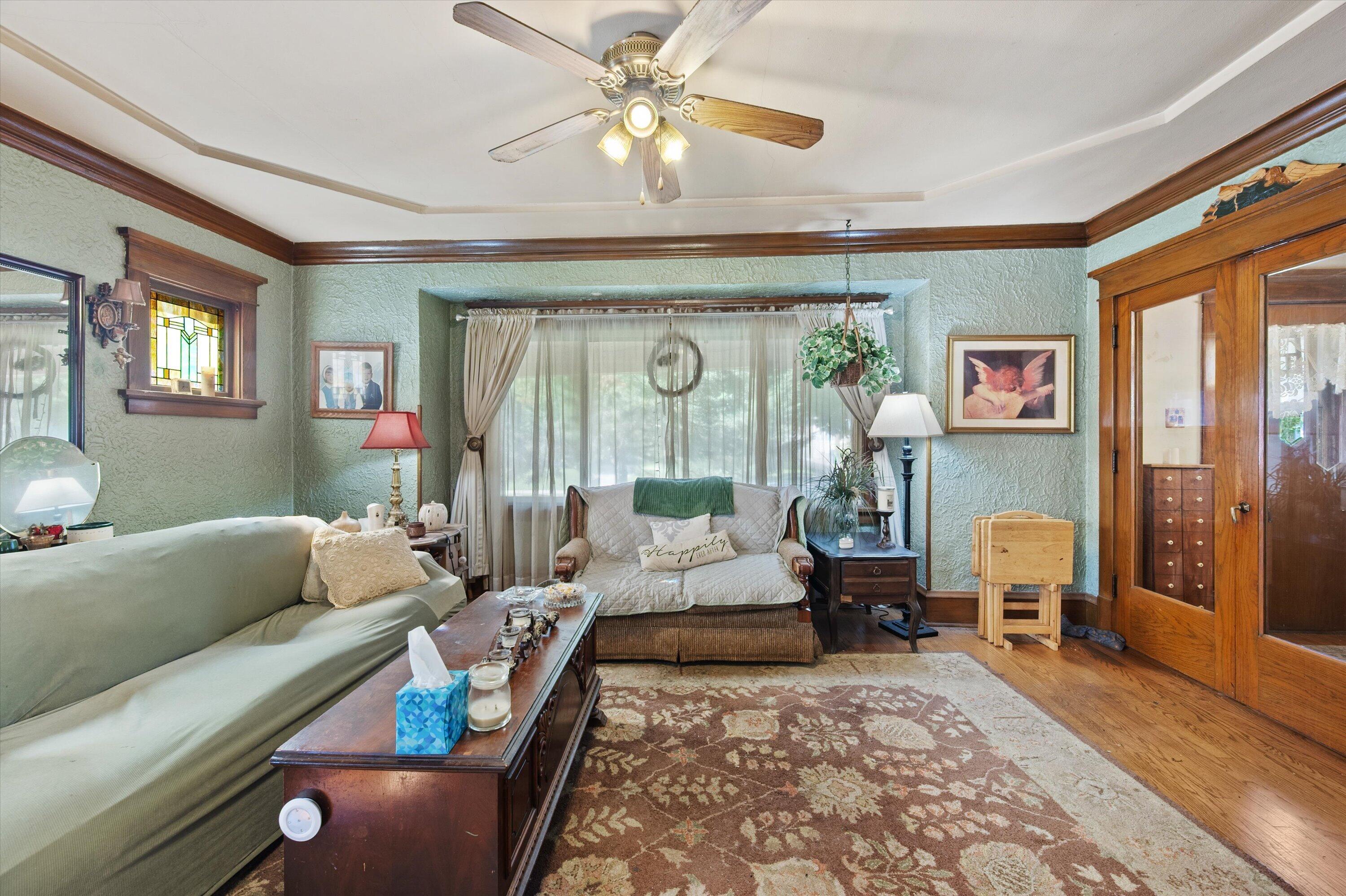 Living room with green seating, ornate wood trim, a stained-glass window and patterned rug.