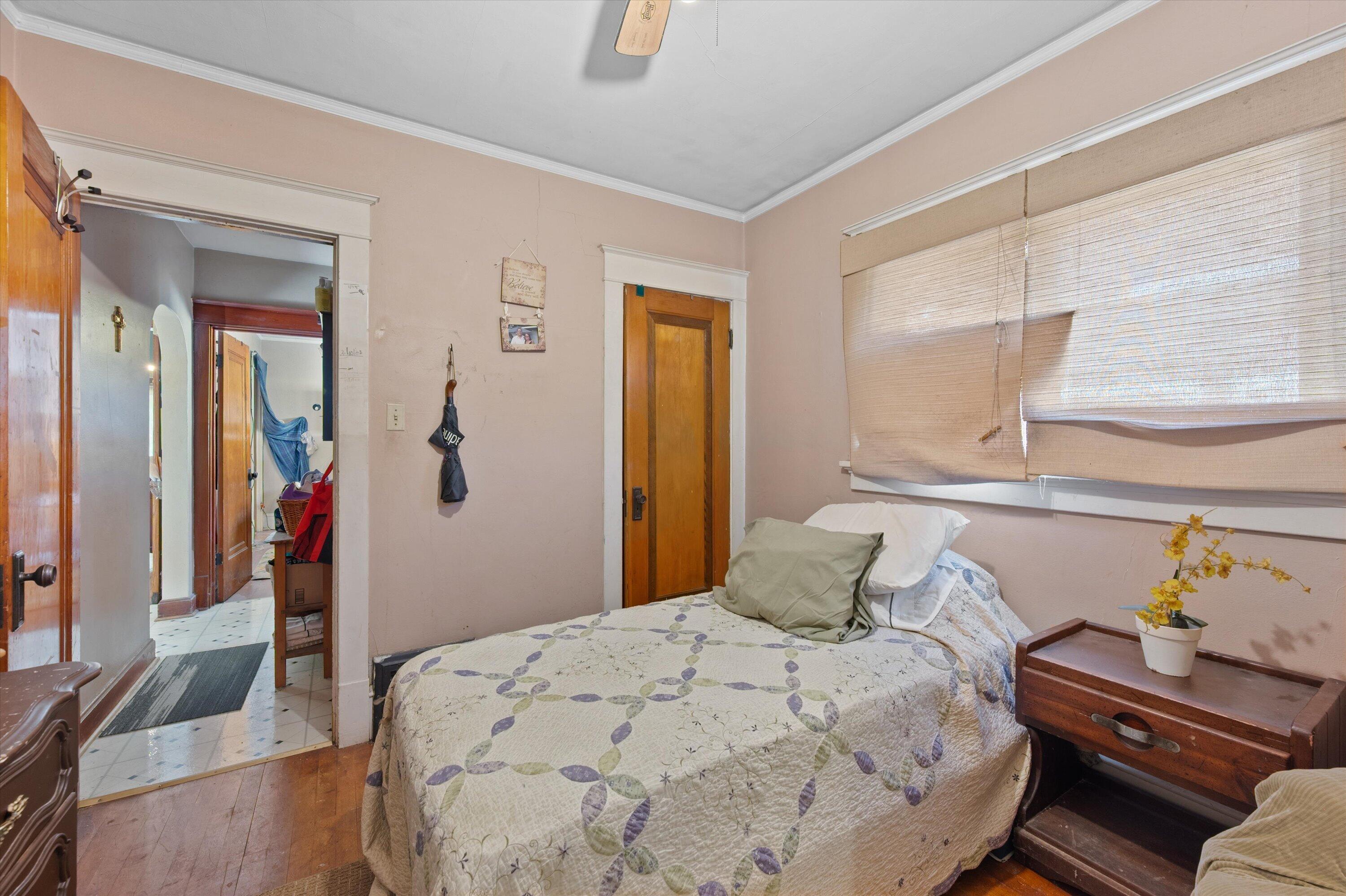 Bedroom with a patterned bed, wood floors, and a large window with beige blinds.