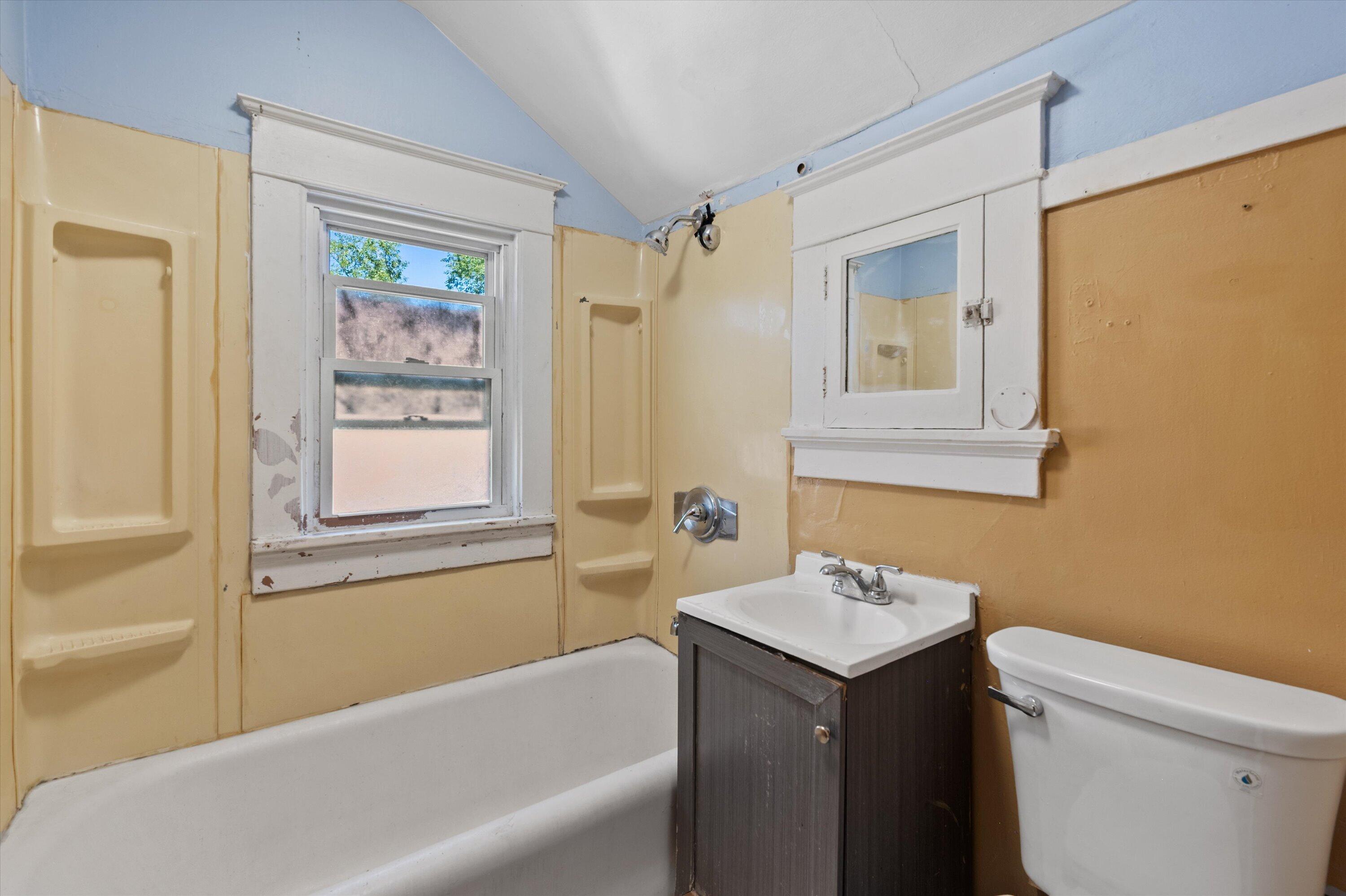 Bathroom with a white tub beneath a window, dark vanity, and toilet.