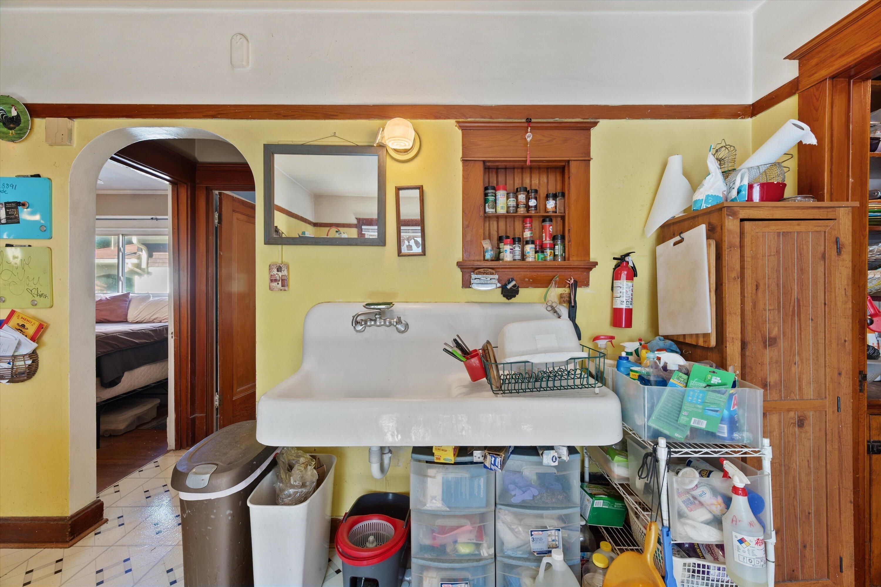 Utility room with a large laundry sink, dark wood cabinets, and cleaning supplies and storage bins.