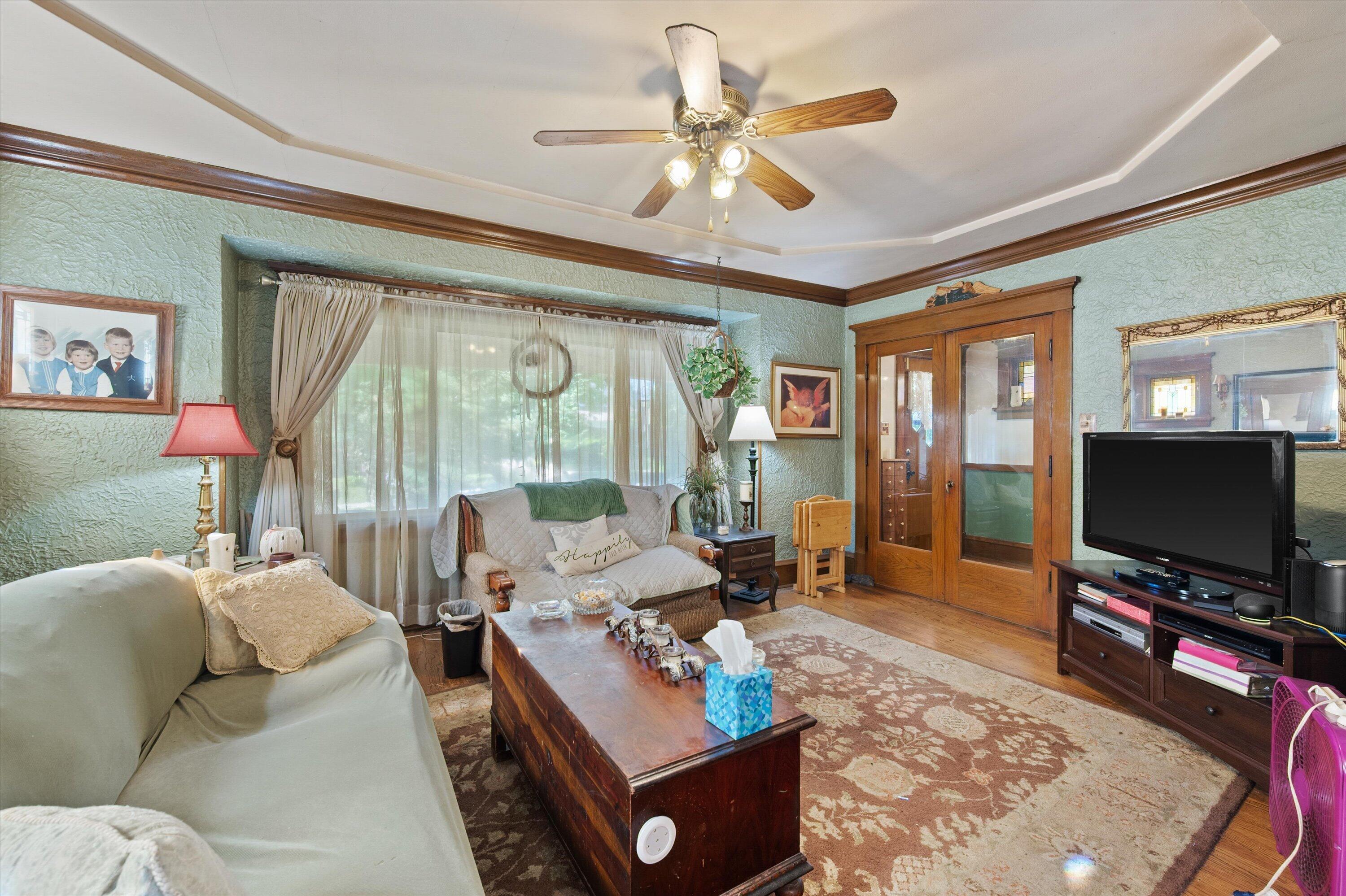 Living room with textured green walls, dark wood trim, sofas, and a ceiling fan.