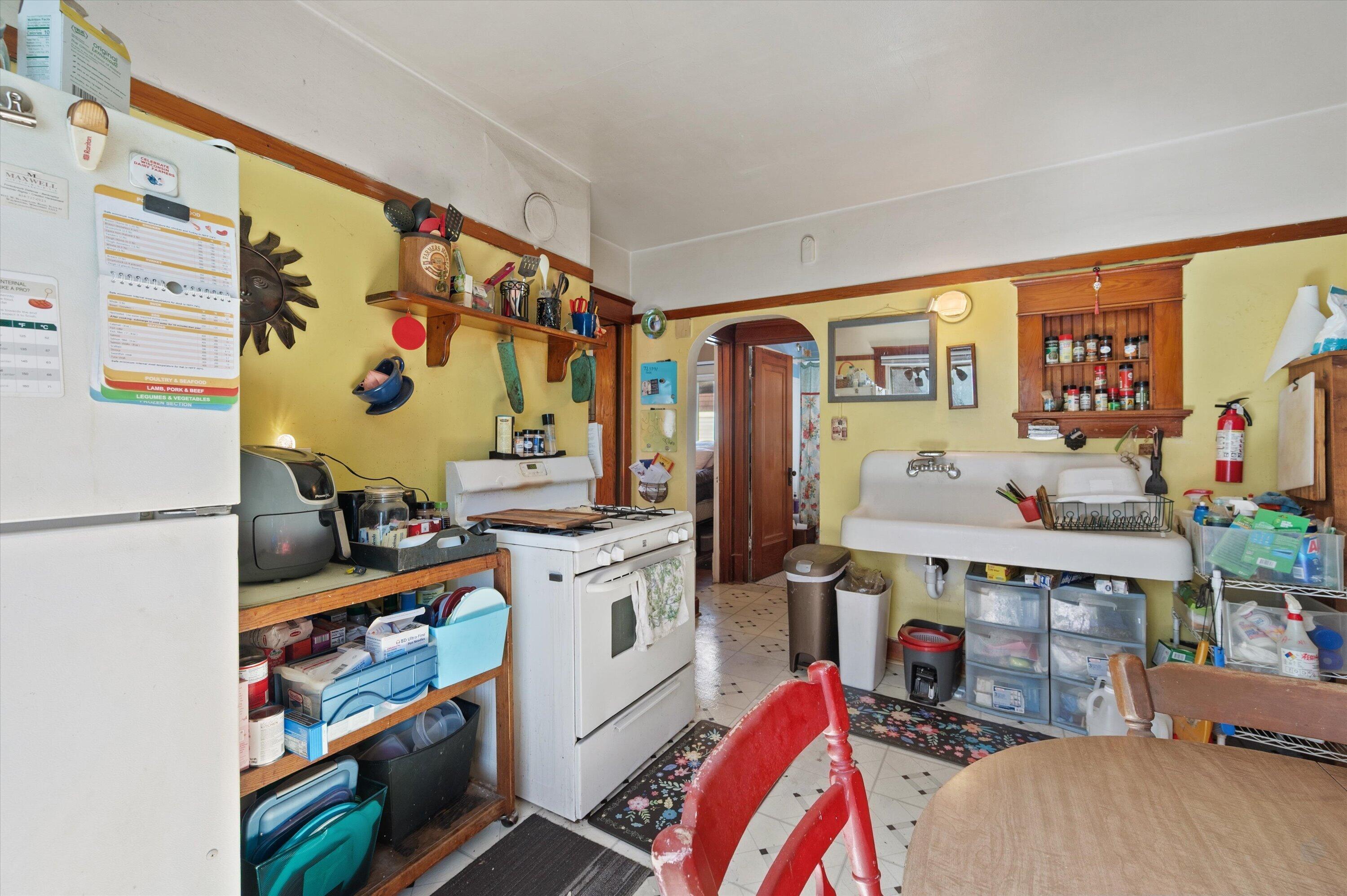 Older kitchen with yellow walls, a white farmhouse sink, vintage stove, and open wooden shelves.