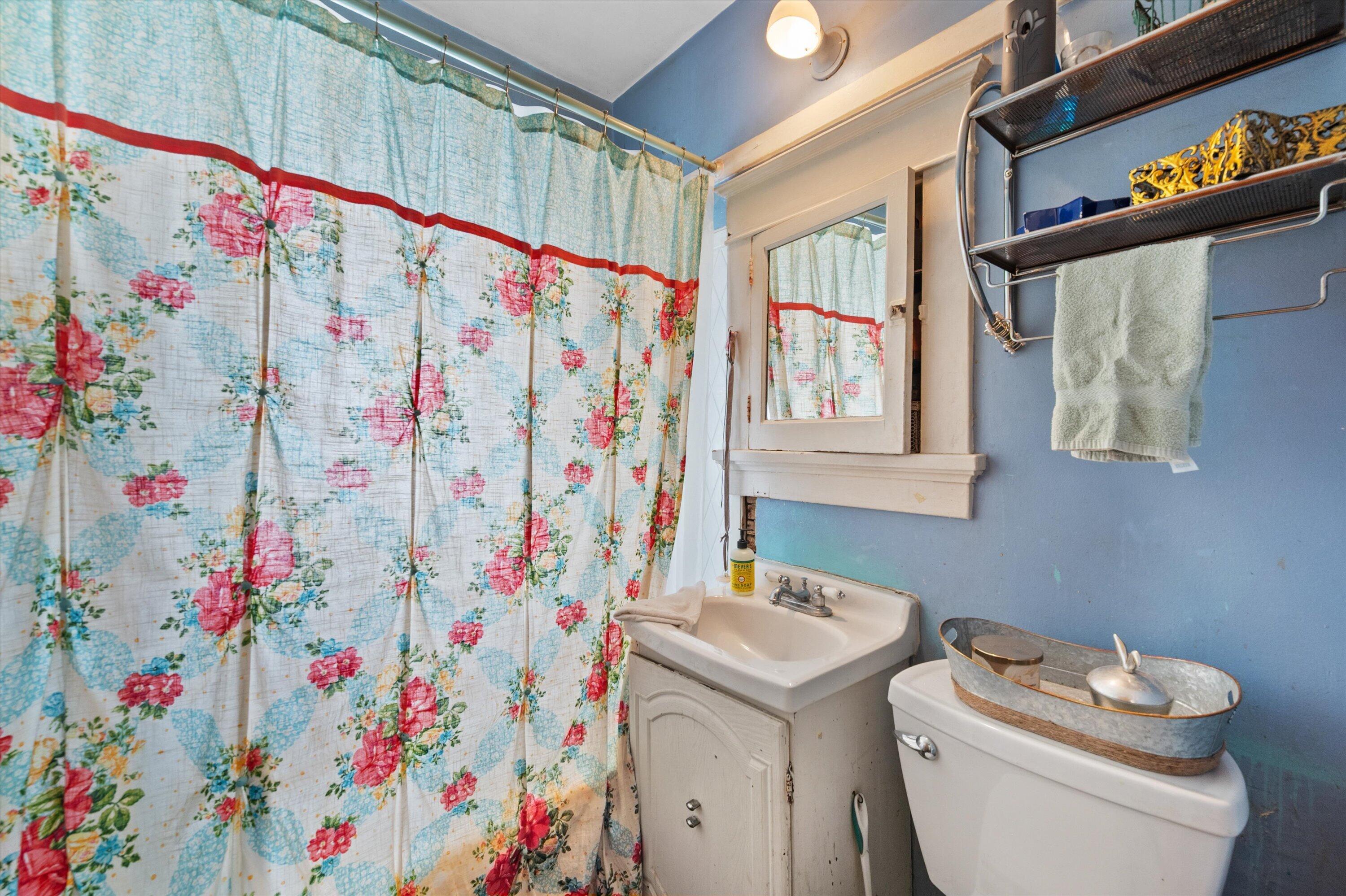 Bathroom with blue walls, floral shower curtain, white sink, and toilet.