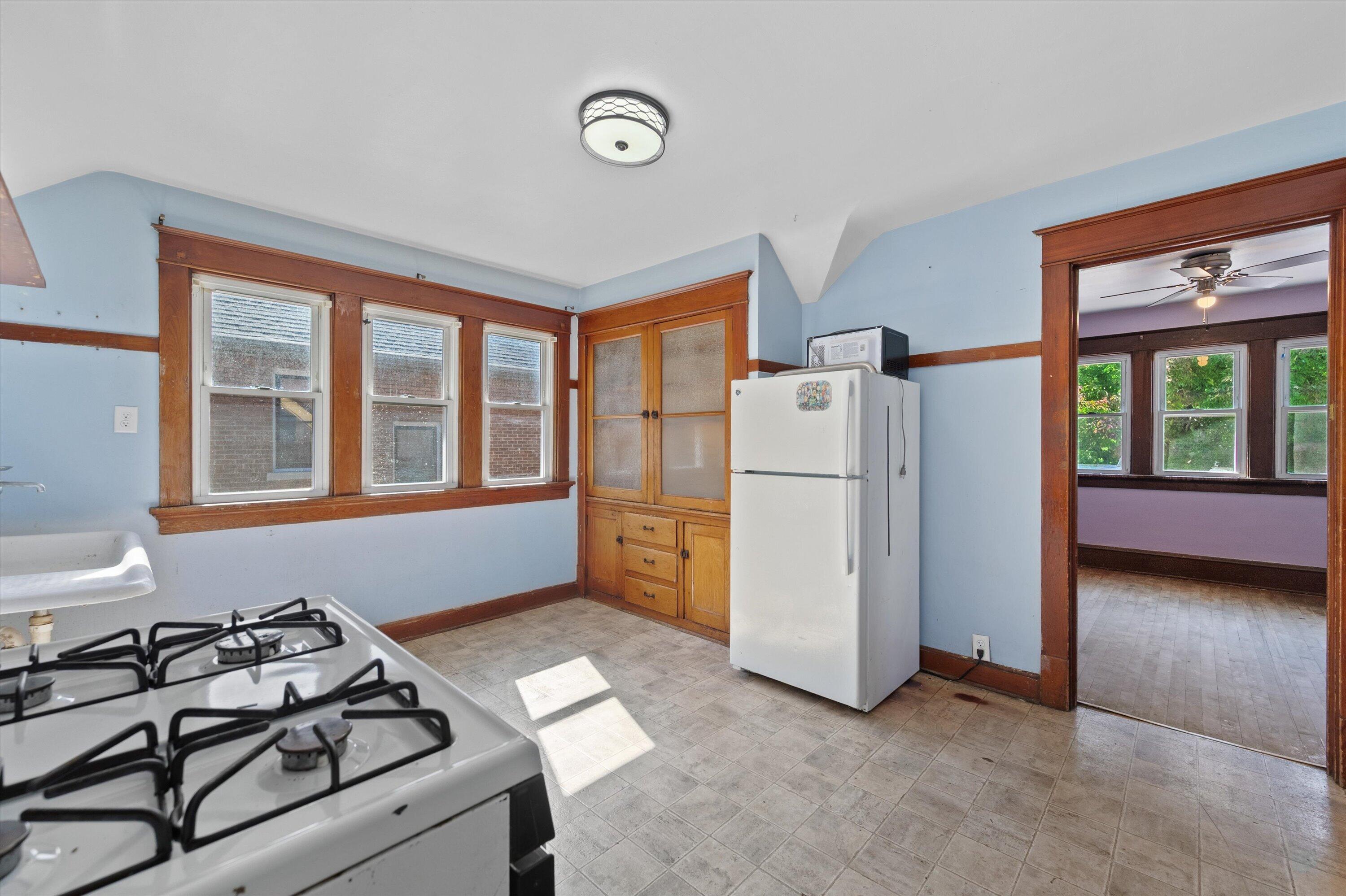 Vacant kitchen with blue walls, wood trim, built-in cabinets, and a doorway to a purple-walled room.