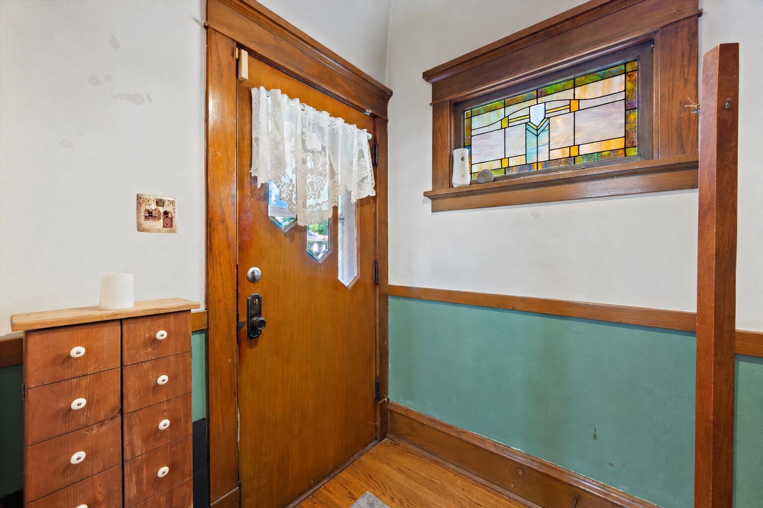 Entryway with a wood front door, lace curtains, and a colorful stained-glass window.