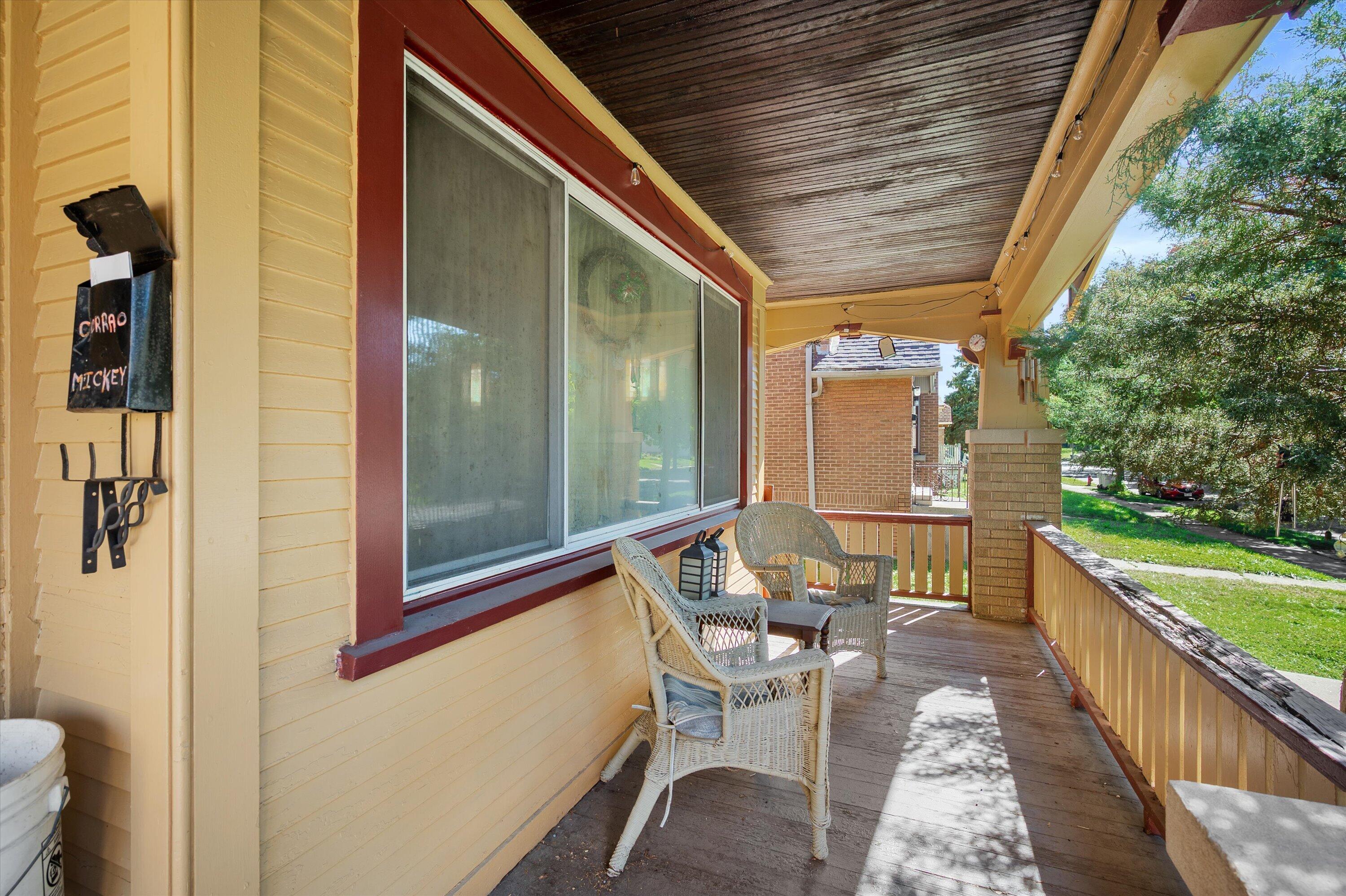 Covered front porch with wicker chairs, yellow siding, and dark red trim.