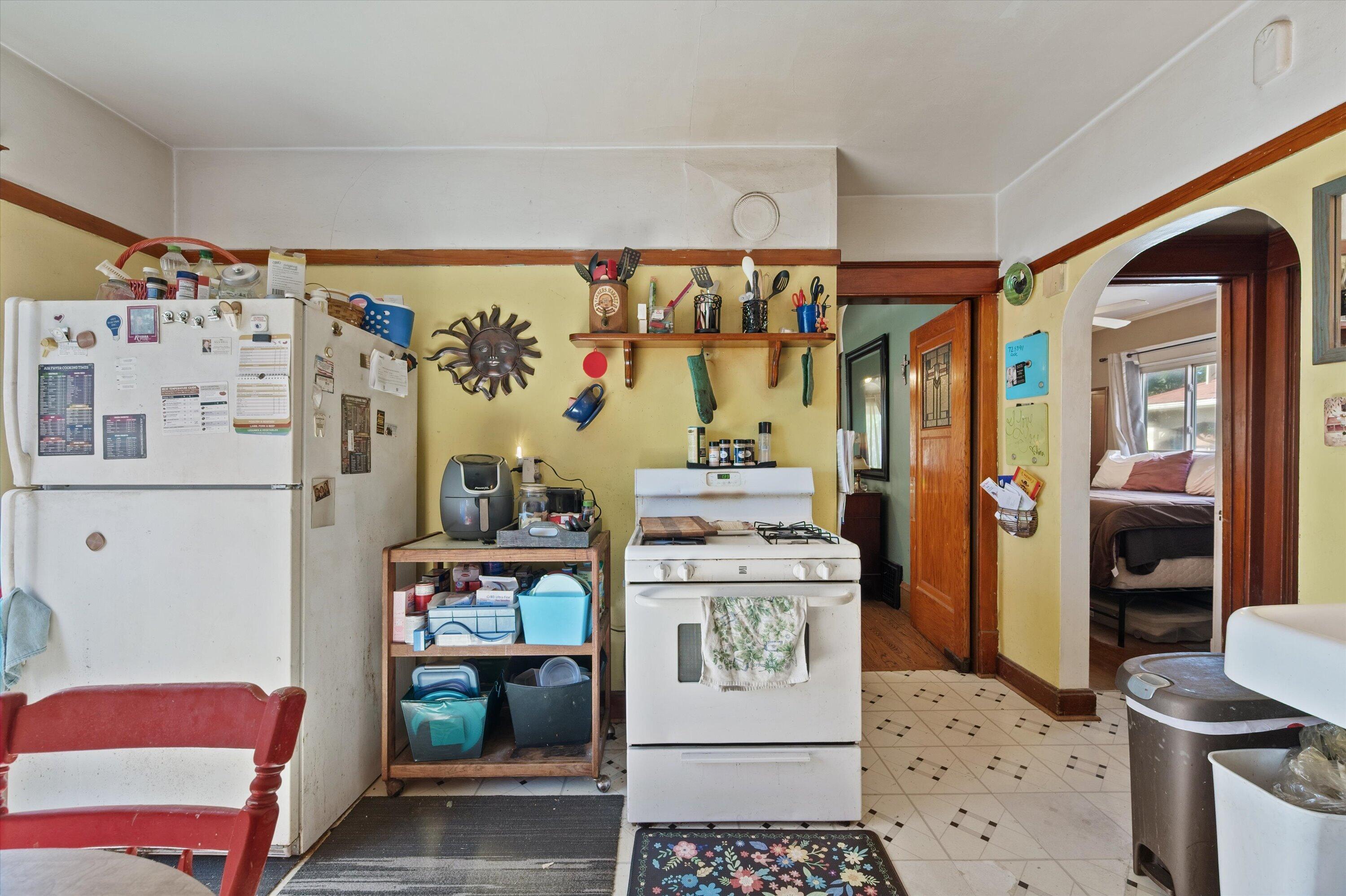 Kitchen with a white gas stove, note-covered refrigerator, and arched doorway to a bedroom.