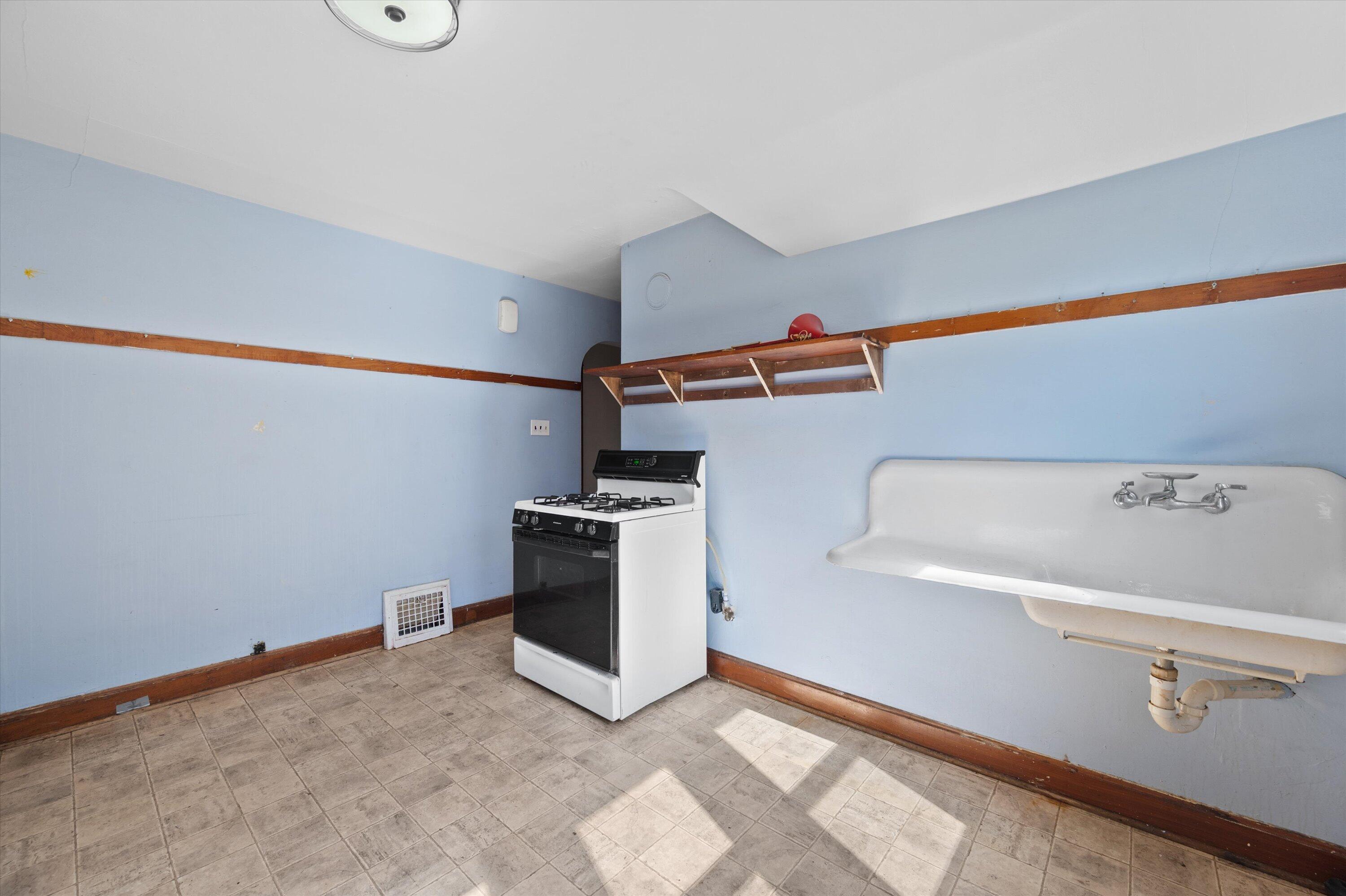 Utility room with a gas range, deep wall-mounted sink, and sunlight across the tiled floor.