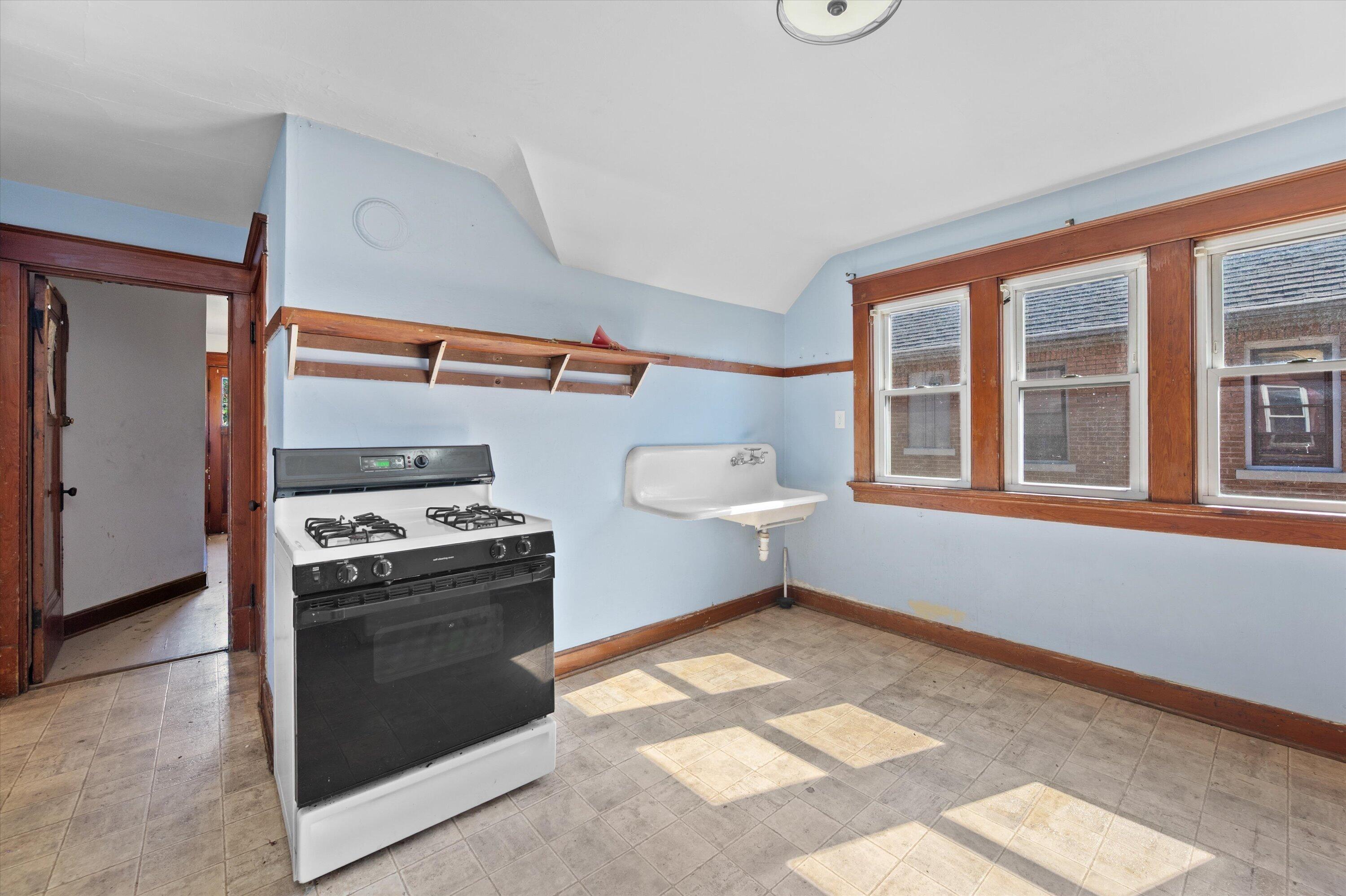Vacant kitchen with a gas range, utility sink, and three wood-trimmed windows.