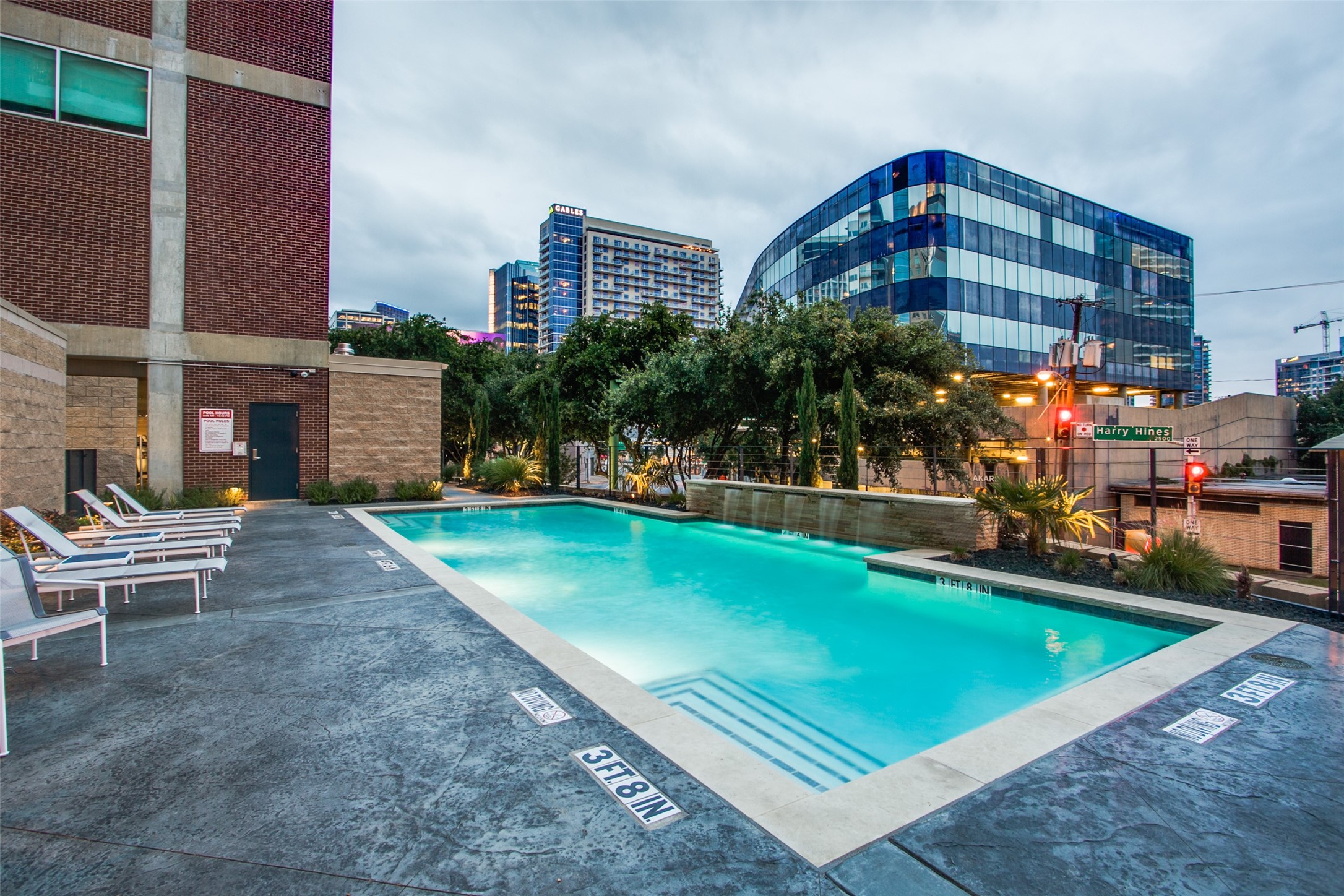 Rooftop swimming pool with white lounge chairs and downtown buildings at dusk.