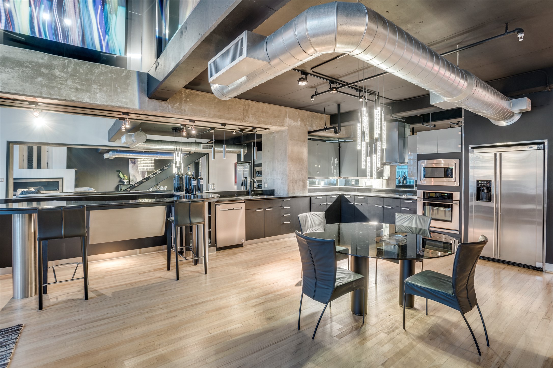 Modern kitchen with dark cabinets, stainless steel appliances, a breakfast bar, and a glass dining table.