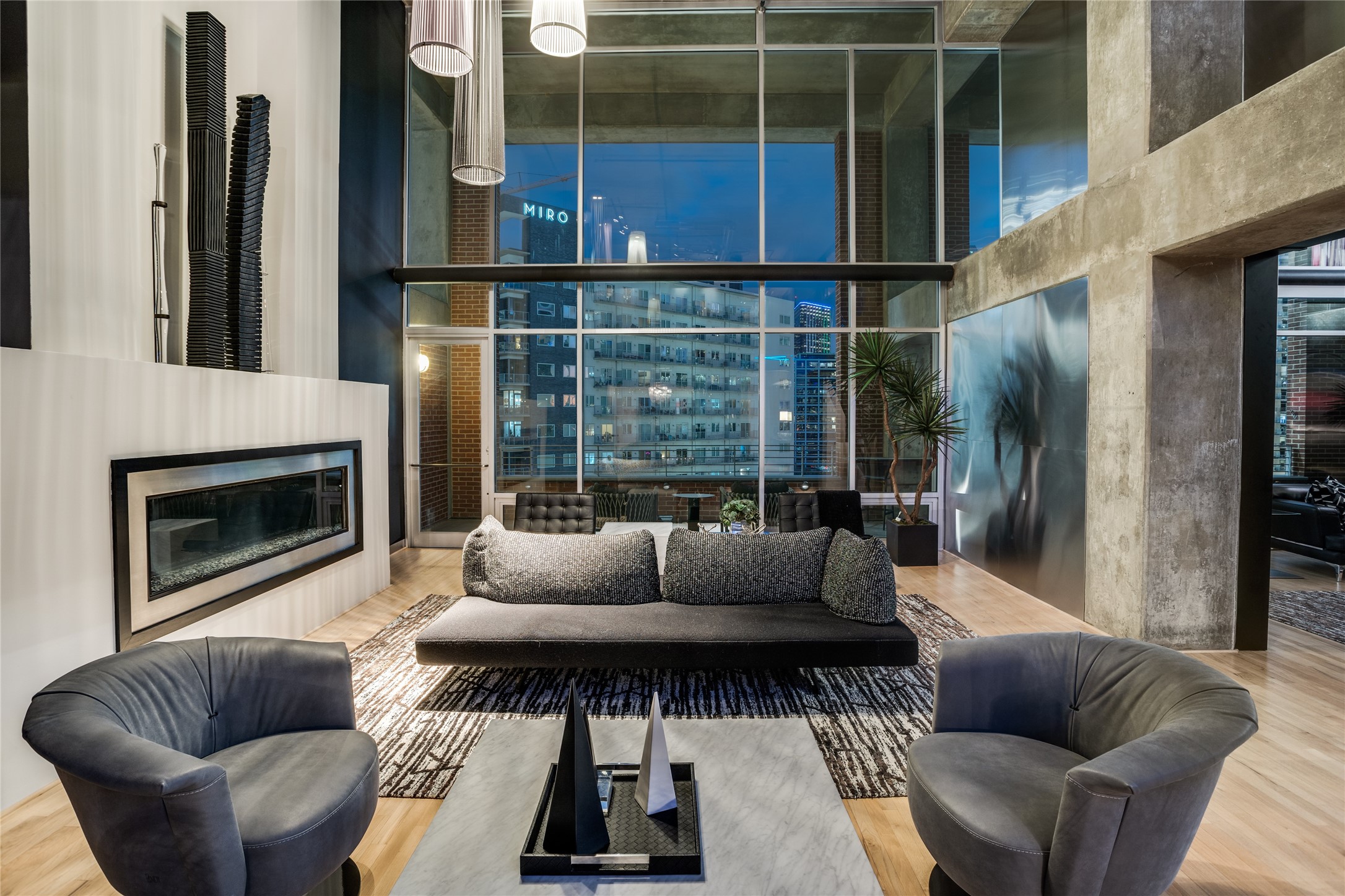 Modern condo living room with floor-to-ceiling windows, a gas fireplace, and downtown views at night.