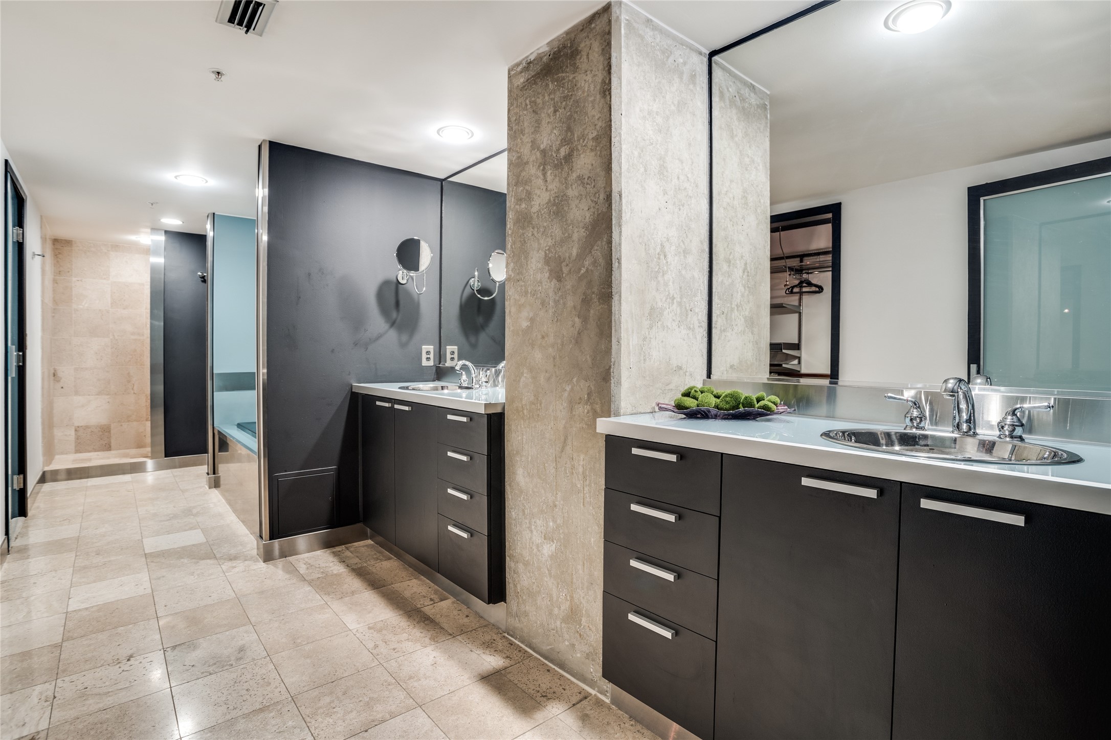 Modern bathroom with a dark double vanity, chrome sinks, large mirrors, and a glass-enclosed shower.