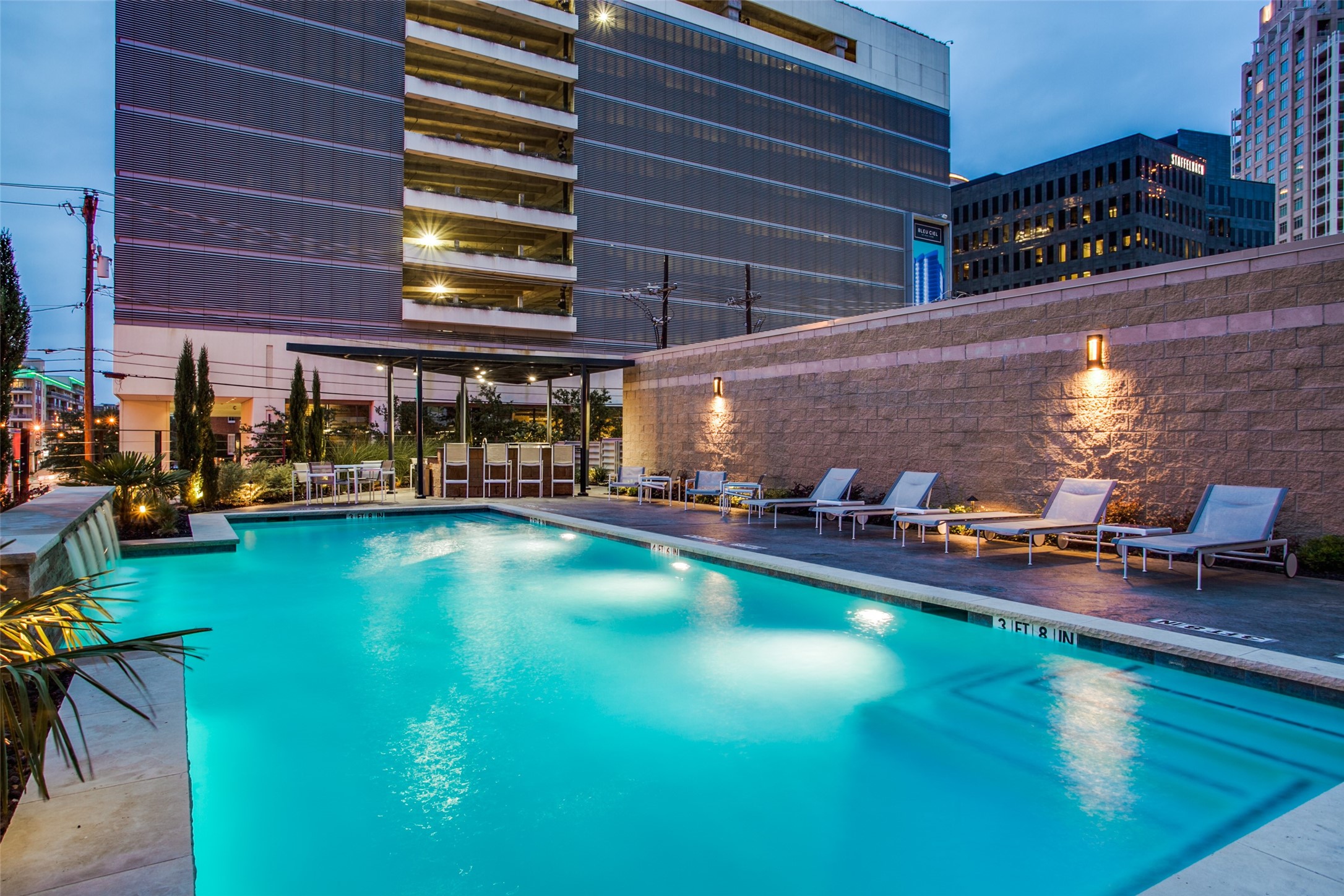 Downtown residential pool at dusk, with lounge chairs beside the illuminated water.