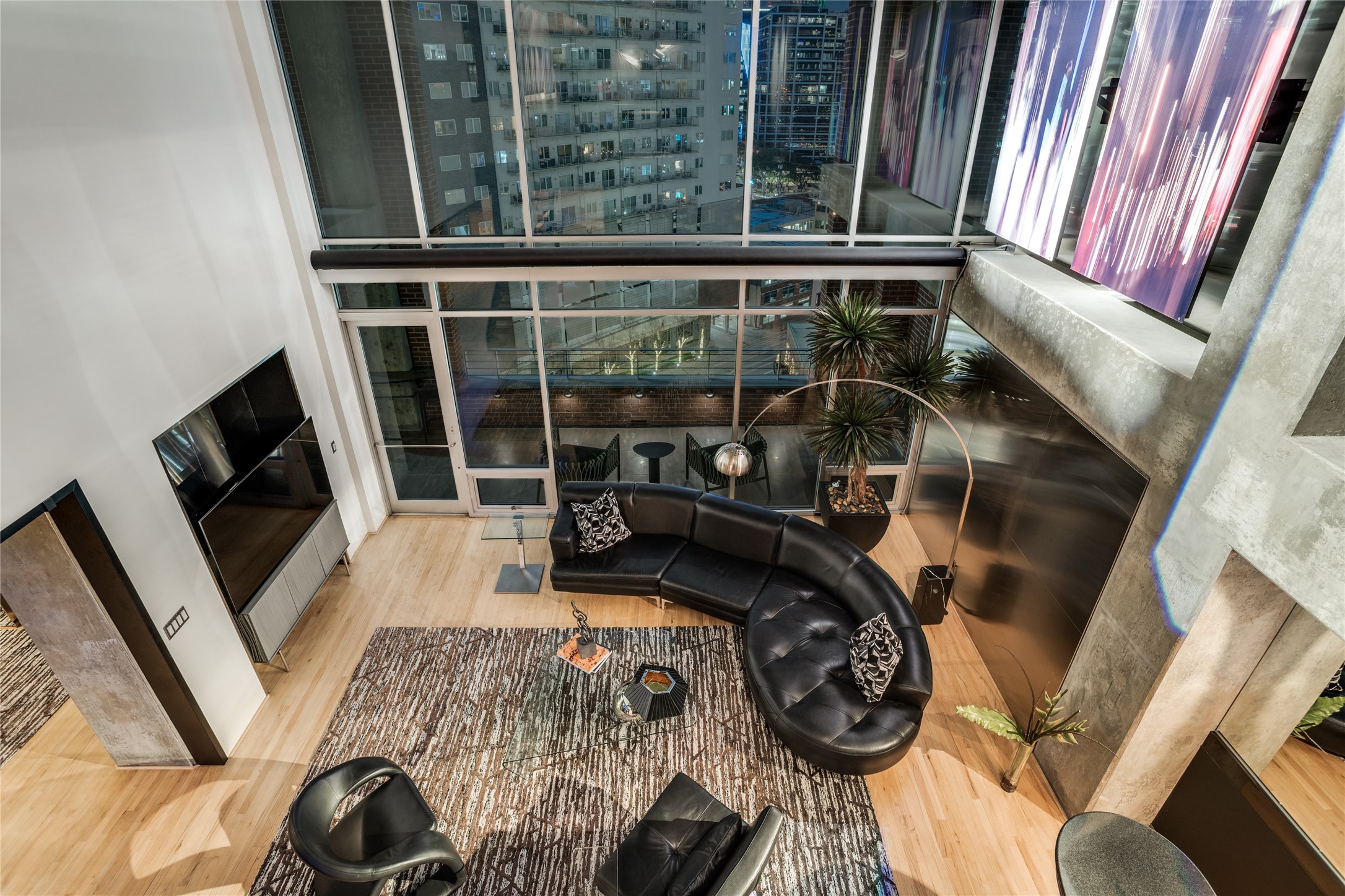 Modern condo living room with a curved black sectional, floor-to-ceiling windows, and city views.
