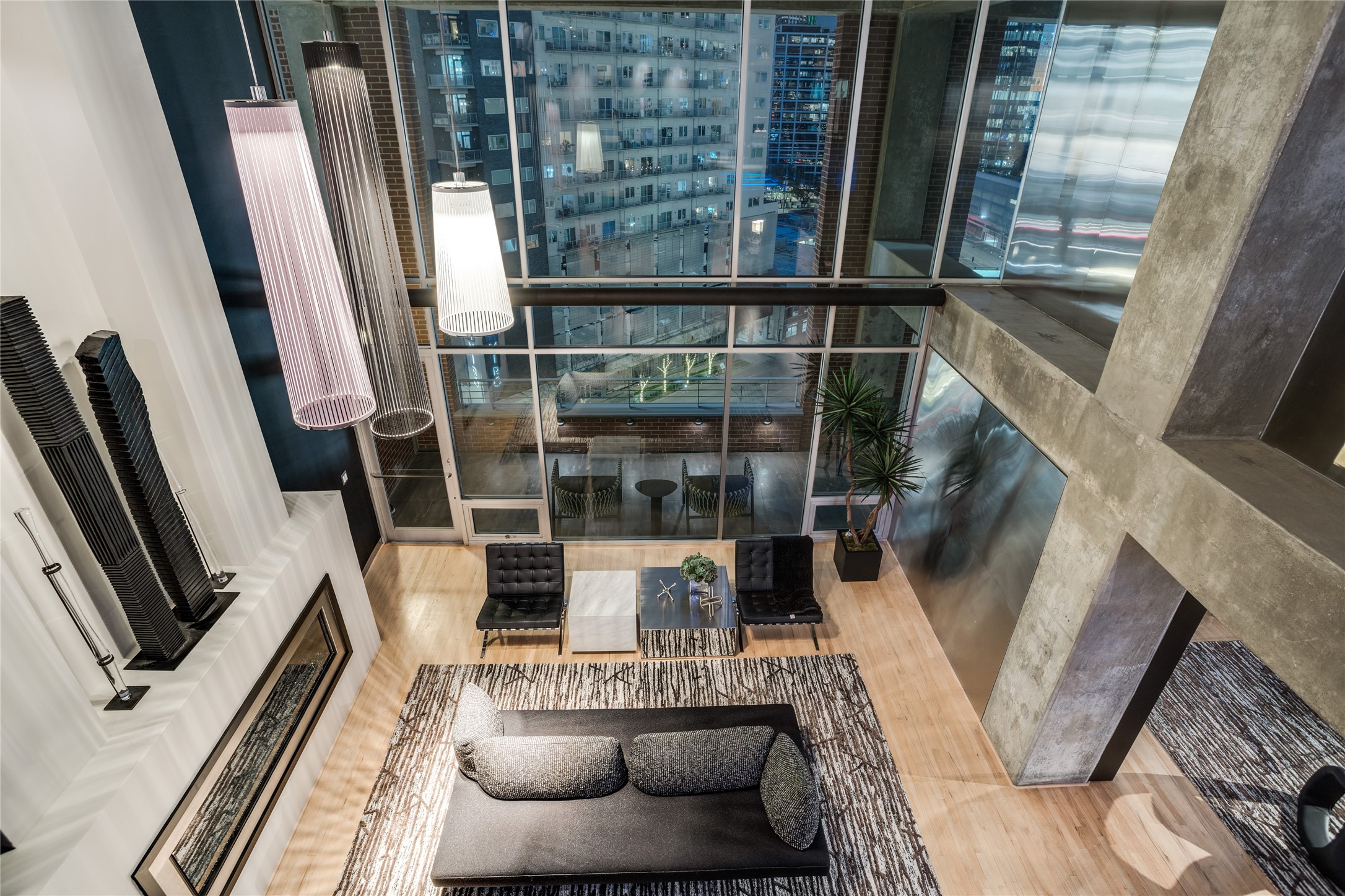 Double-height condo living room with floor-to-ceiling windows overlooking the illuminated city.