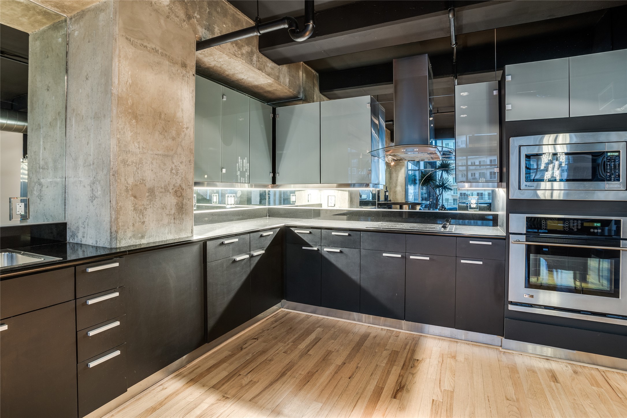 Modern kitchen with dark cabinetry, stainless steel appliances, and exposed concrete columns.