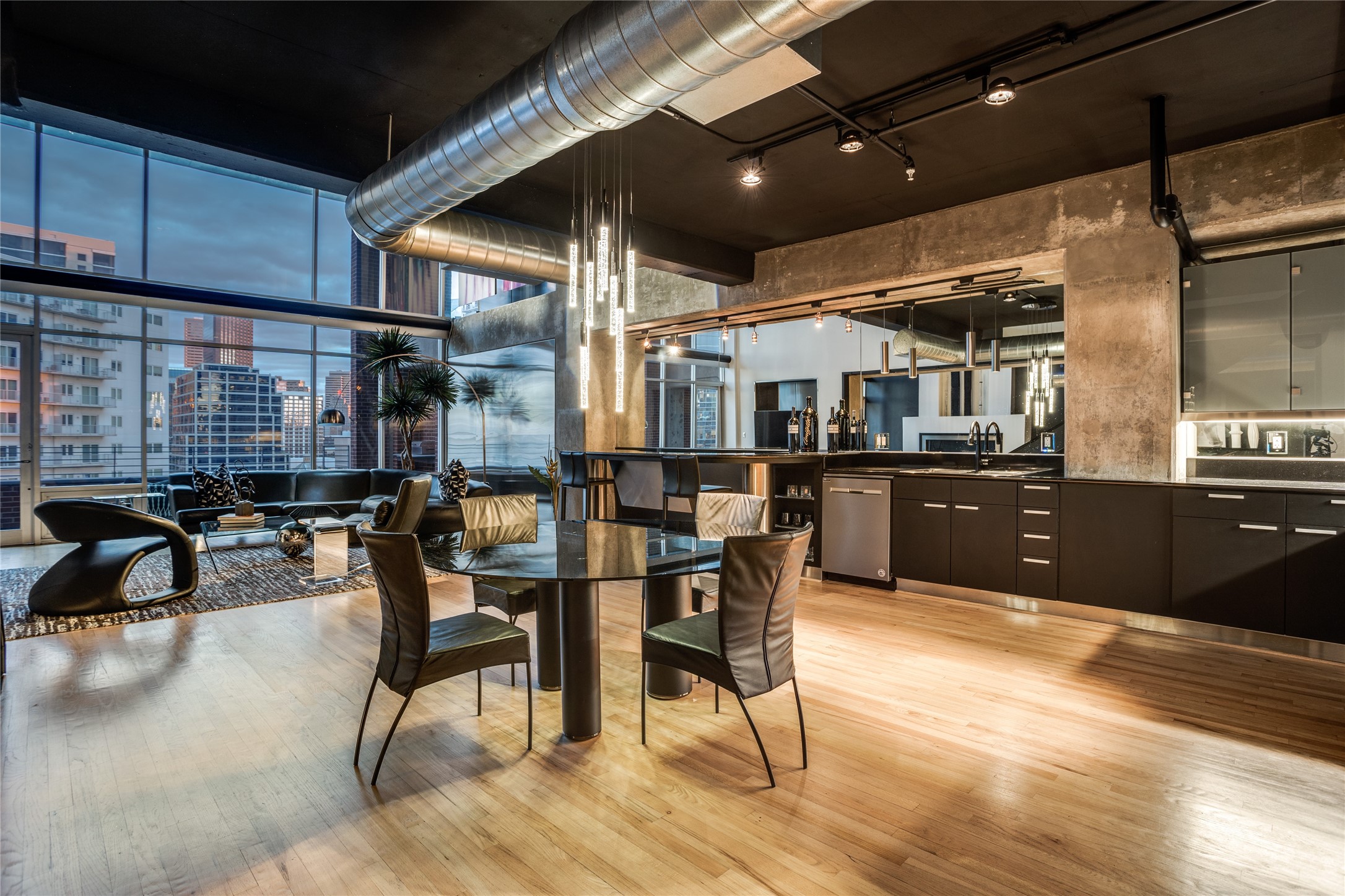 Open-plan condo living and dining area with a modern kitchen, exposed ductwork, and city views.