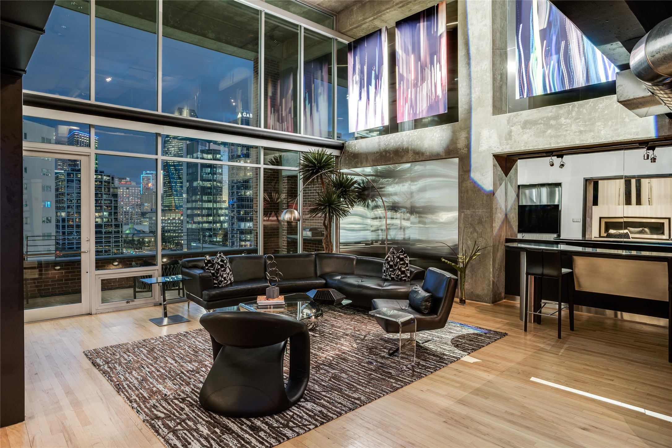 Loft living room with floor-to-ceiling city views, a black leather sectional, and exposed concrete.