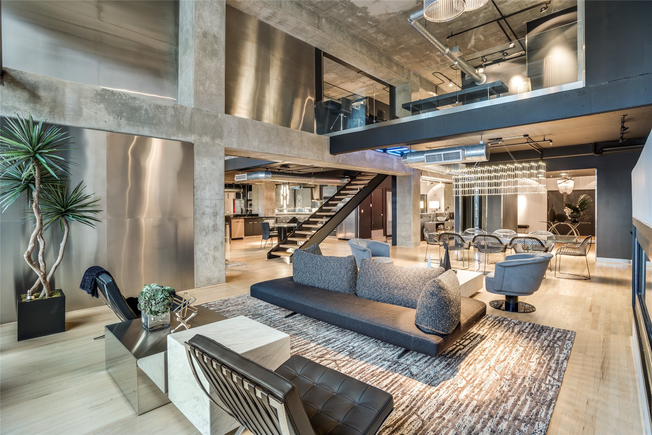 Modern loft living area with exposed concrete, open staircase, upper level, and dining area.