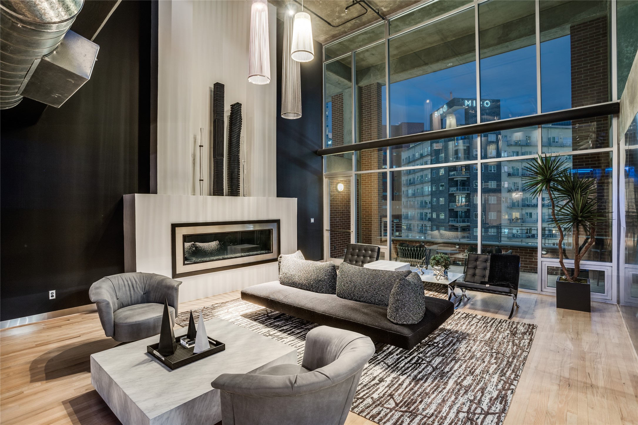 Modern living room with a linear fireplace, floor-to-ceiling windows, and city views at dusk.