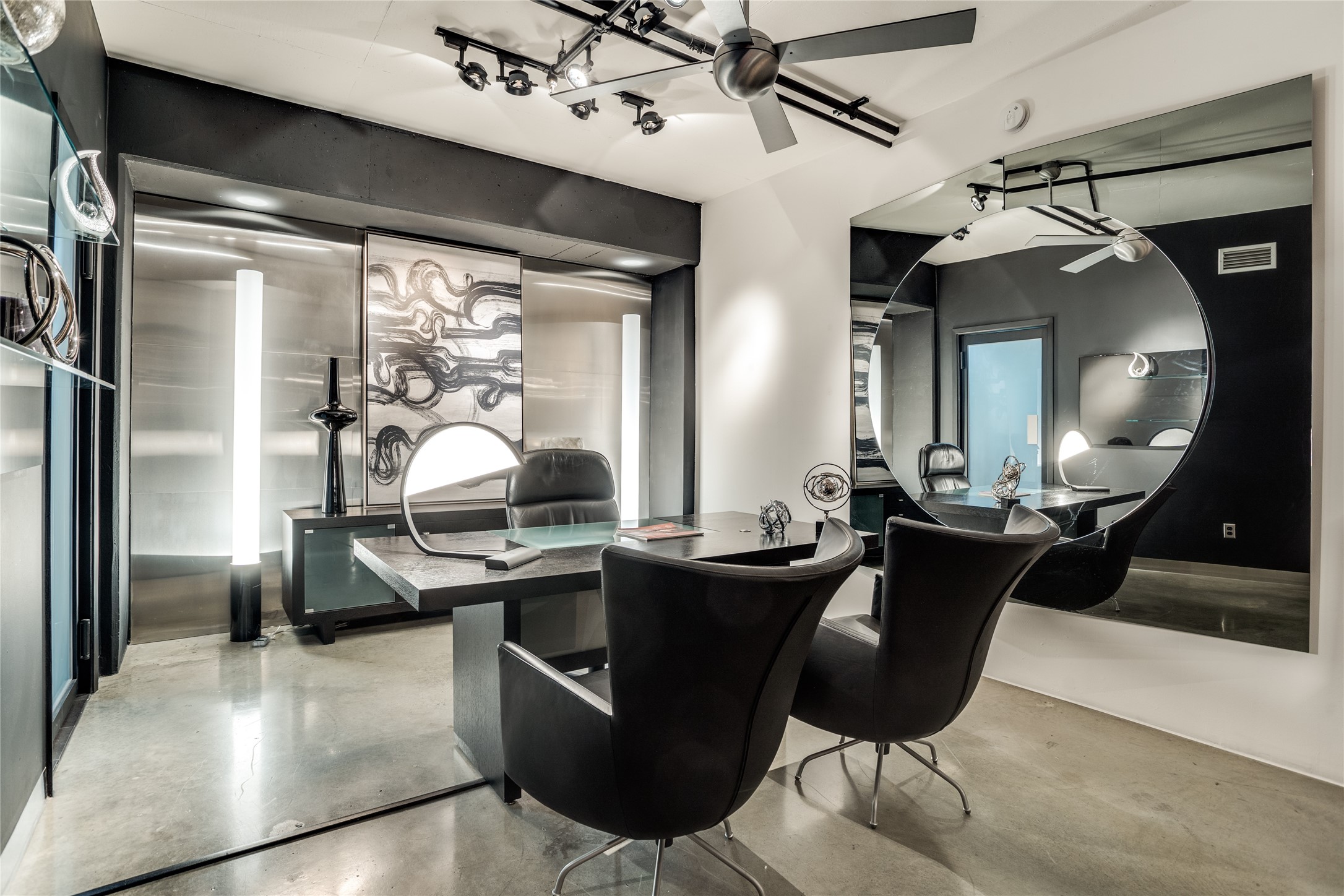 Modern office with a dark desk, black leather chairs, and an oversized mirrored wall.