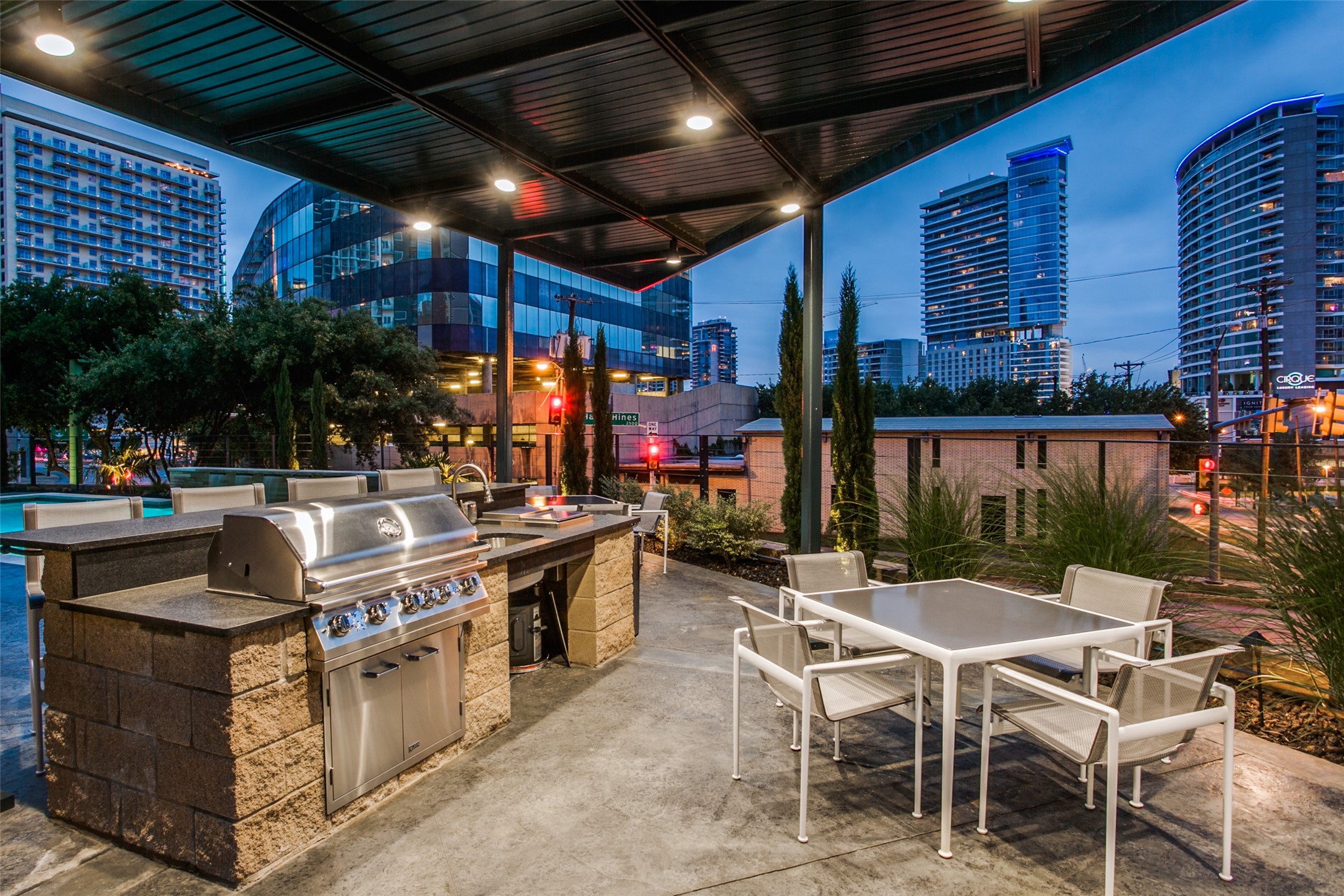 Rooftop patio with a covered grill station and dining table overlooking high-rise buildings.