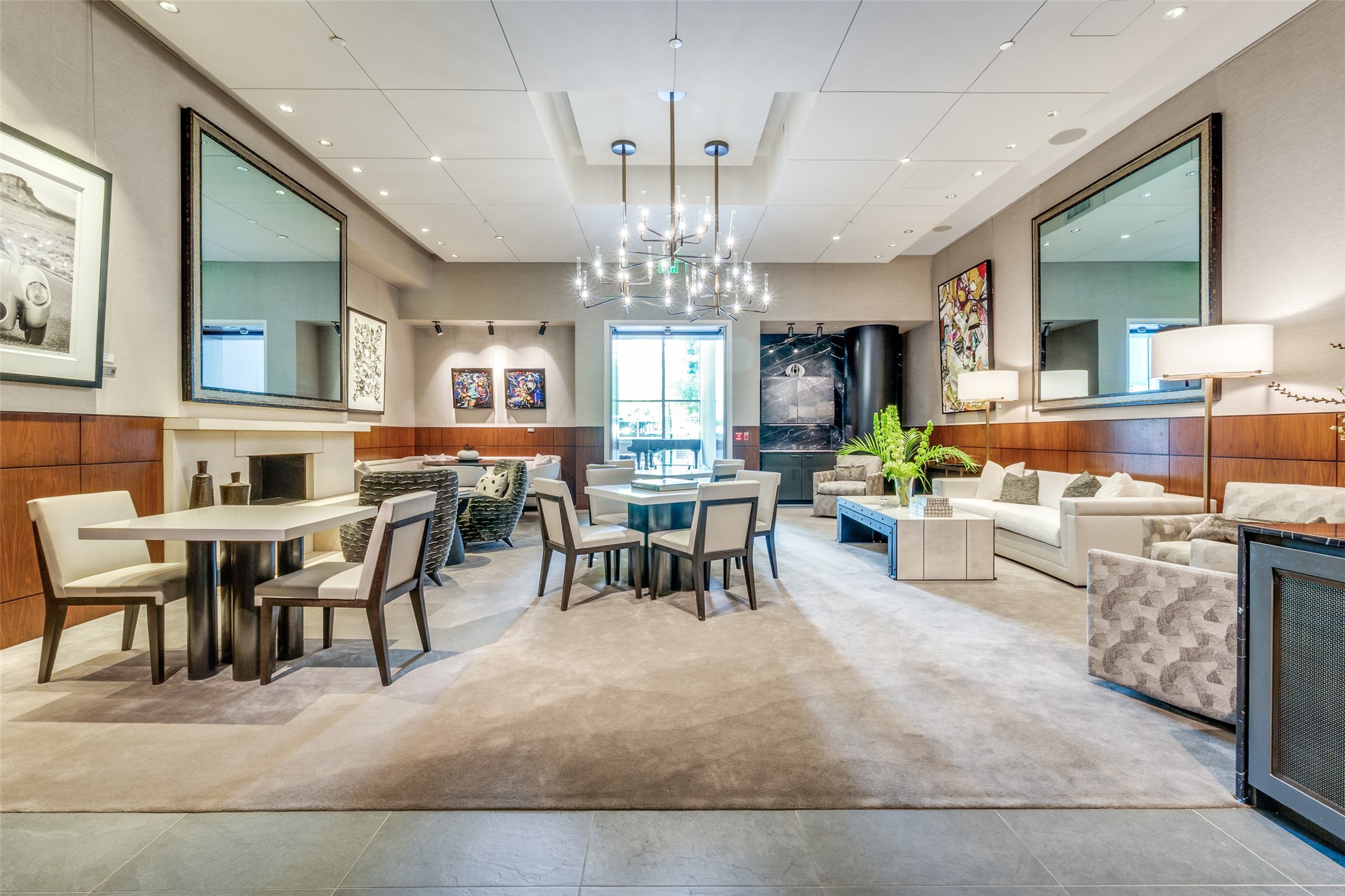 Furnished lounge with dining tables, white sofas, a fireplace, and a large modern chandelier.