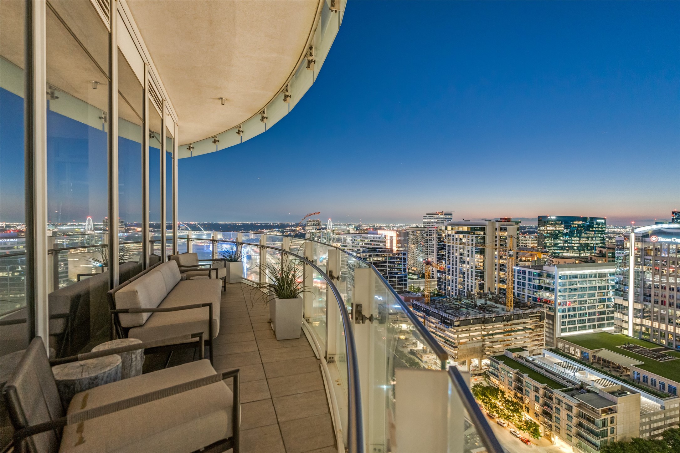 High-rise balcony with lounge seating and glass railing overlooking the downtown Dallas skyline at dusk.
