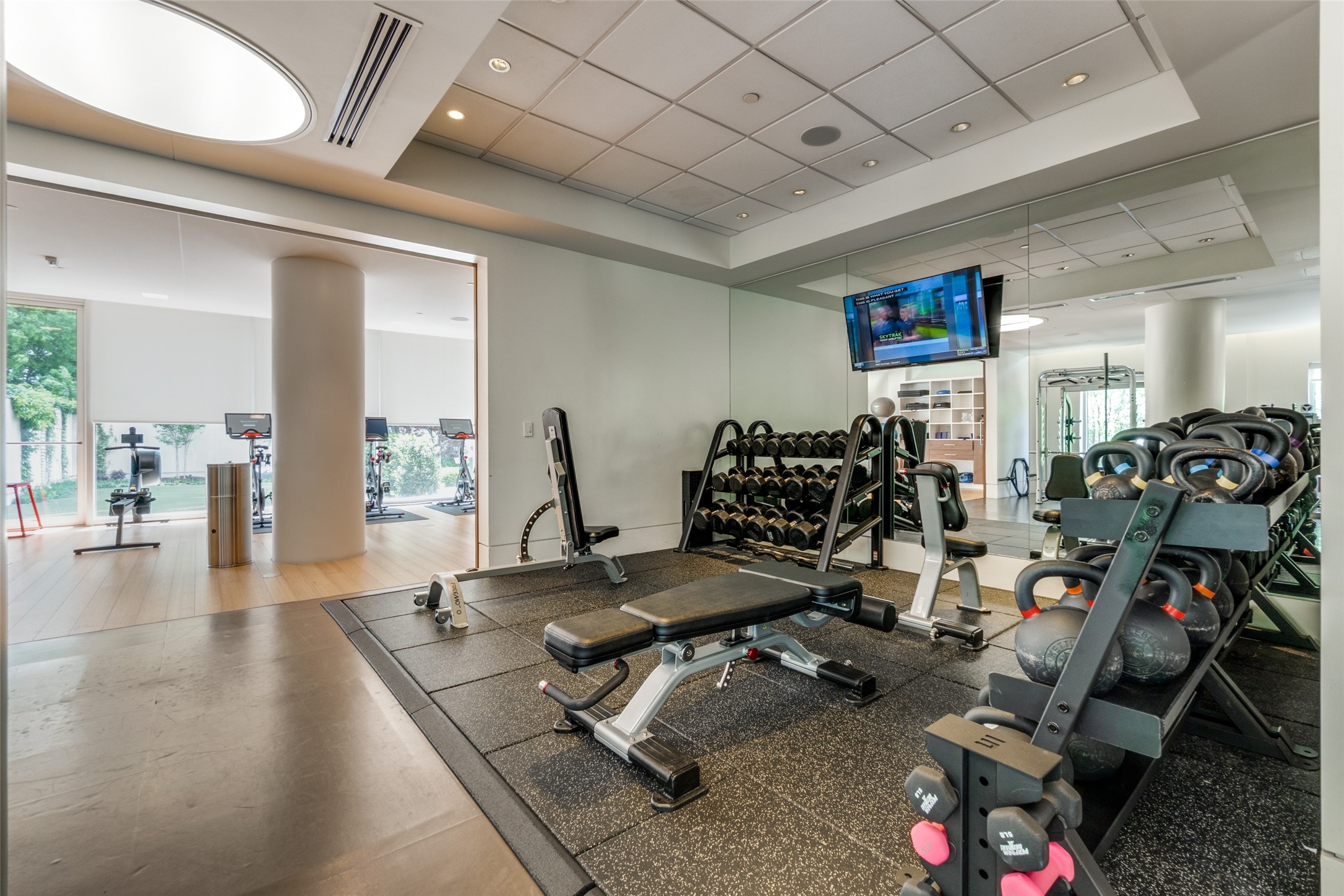 Fitness center with mirrored walls, rows of weights, kettlebells, and workout benches.