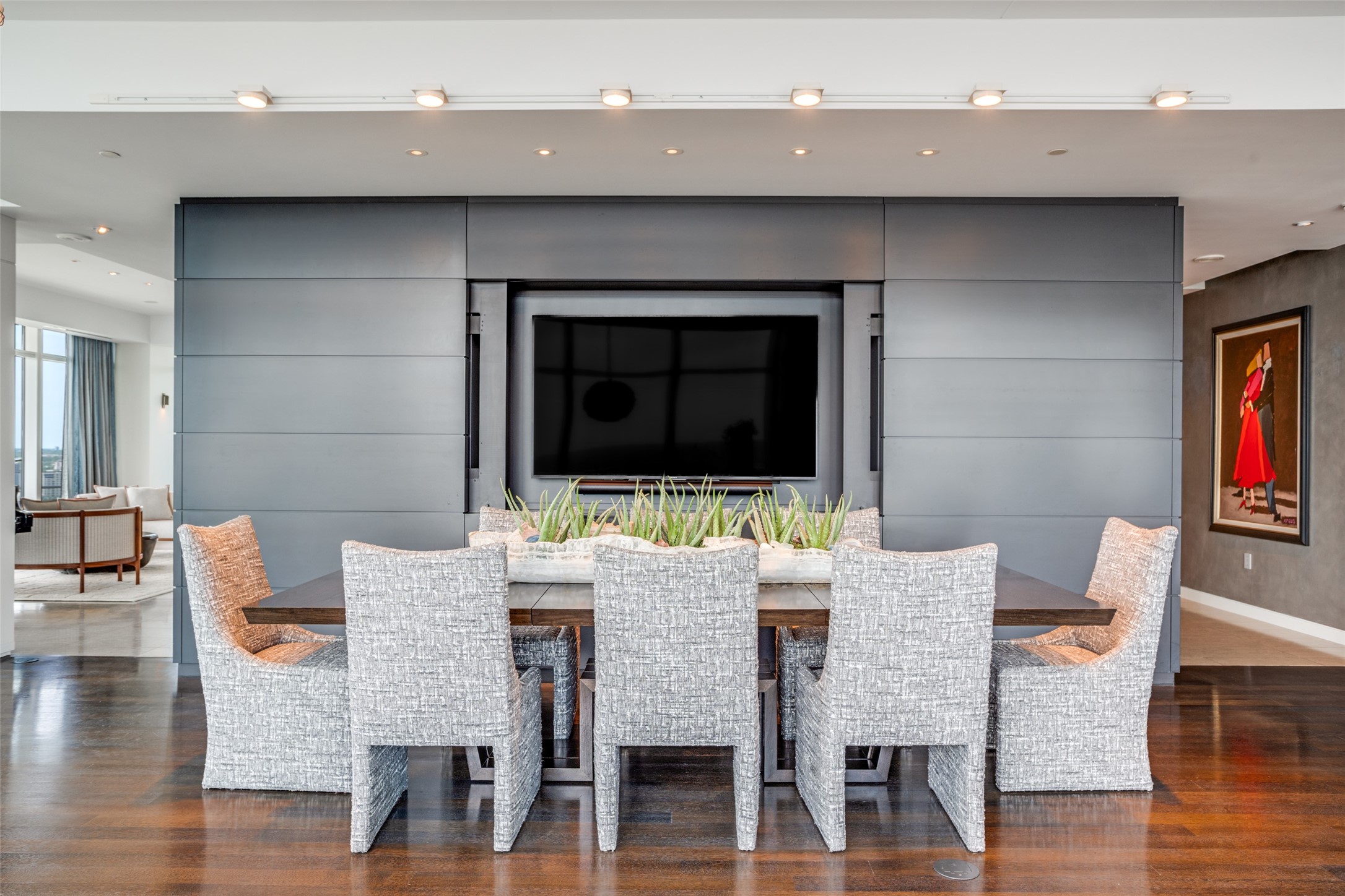 Dining room with woven chairs, a planter centerpiece, and a television on a paneled wall.