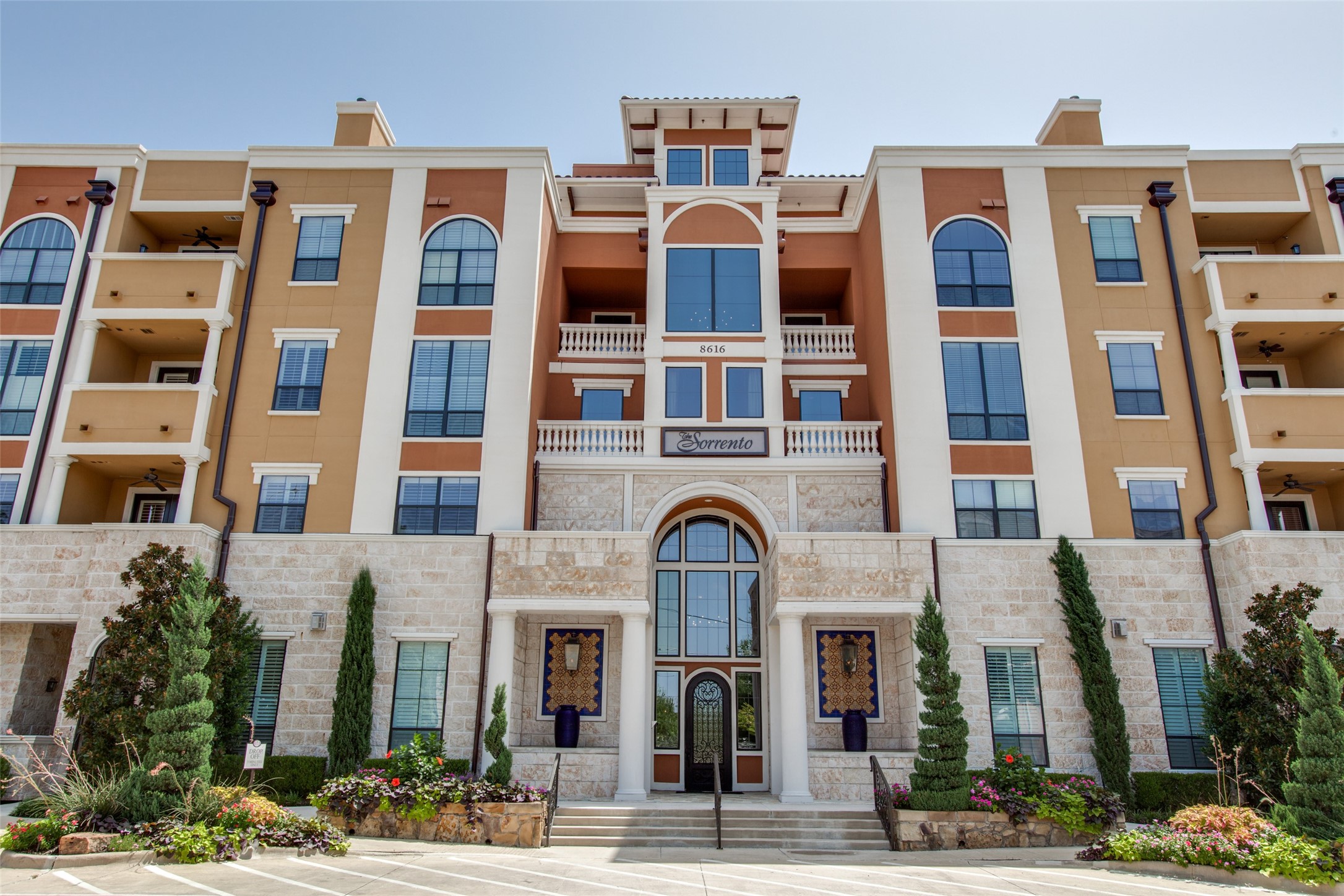 The Sorrento condominium facade with a stone entry, arched glass doorway, balconies, and landscaped flower beds.