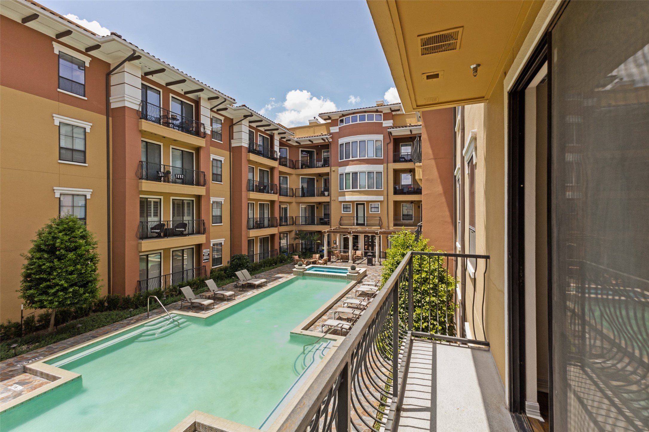 Apartment courtyard pool viewed from a balcony, with surrounding buildings and poolside lounge chairs.