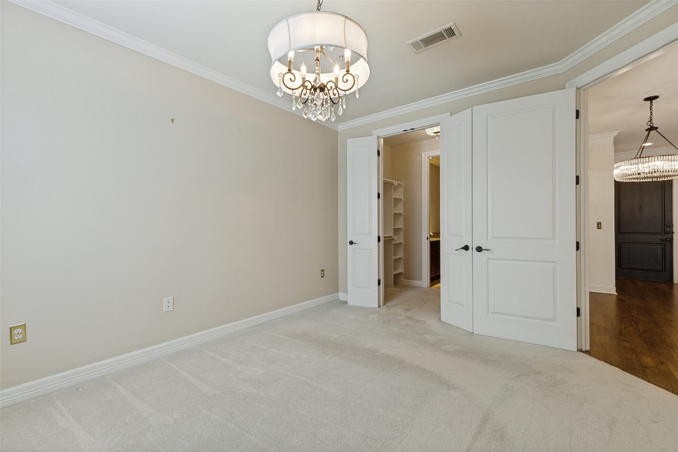Empty carpeted room with a crystal chandelier and open doors to a closet area and hall.