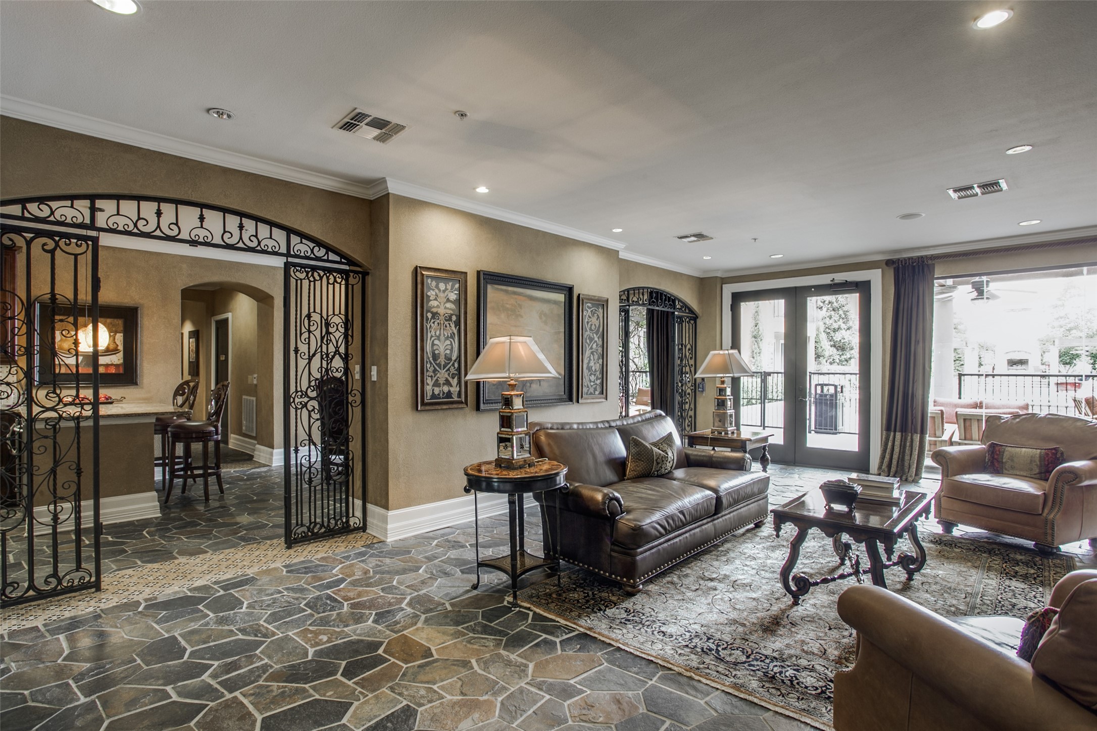 Living room with leather seating, ornate wrought-iron divider, stone tile floors, and doors to a balcony.