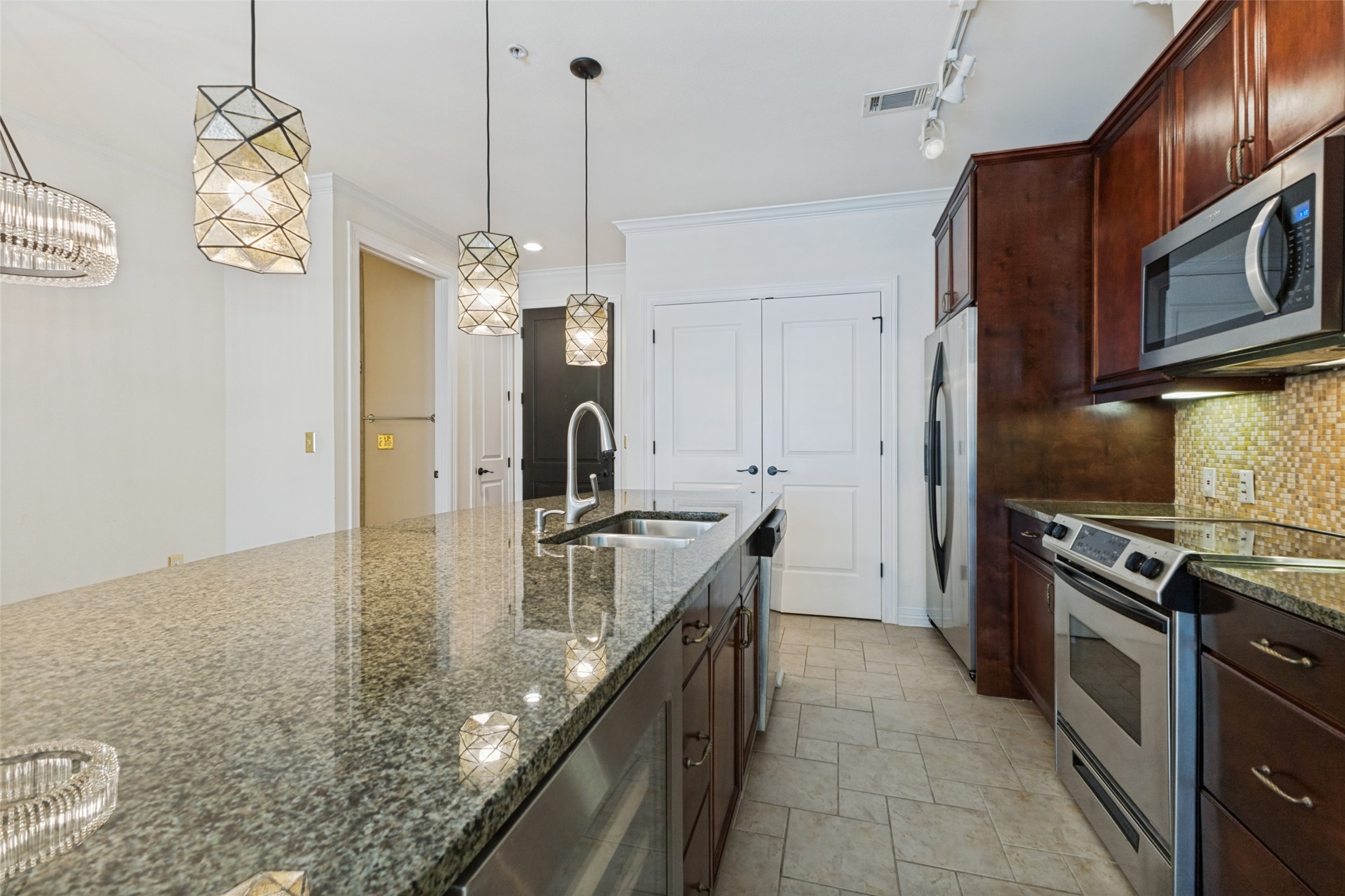 Kitchen with a granite island, dark wood cabinets, stainless steel appliances, and geometric pendant lights.