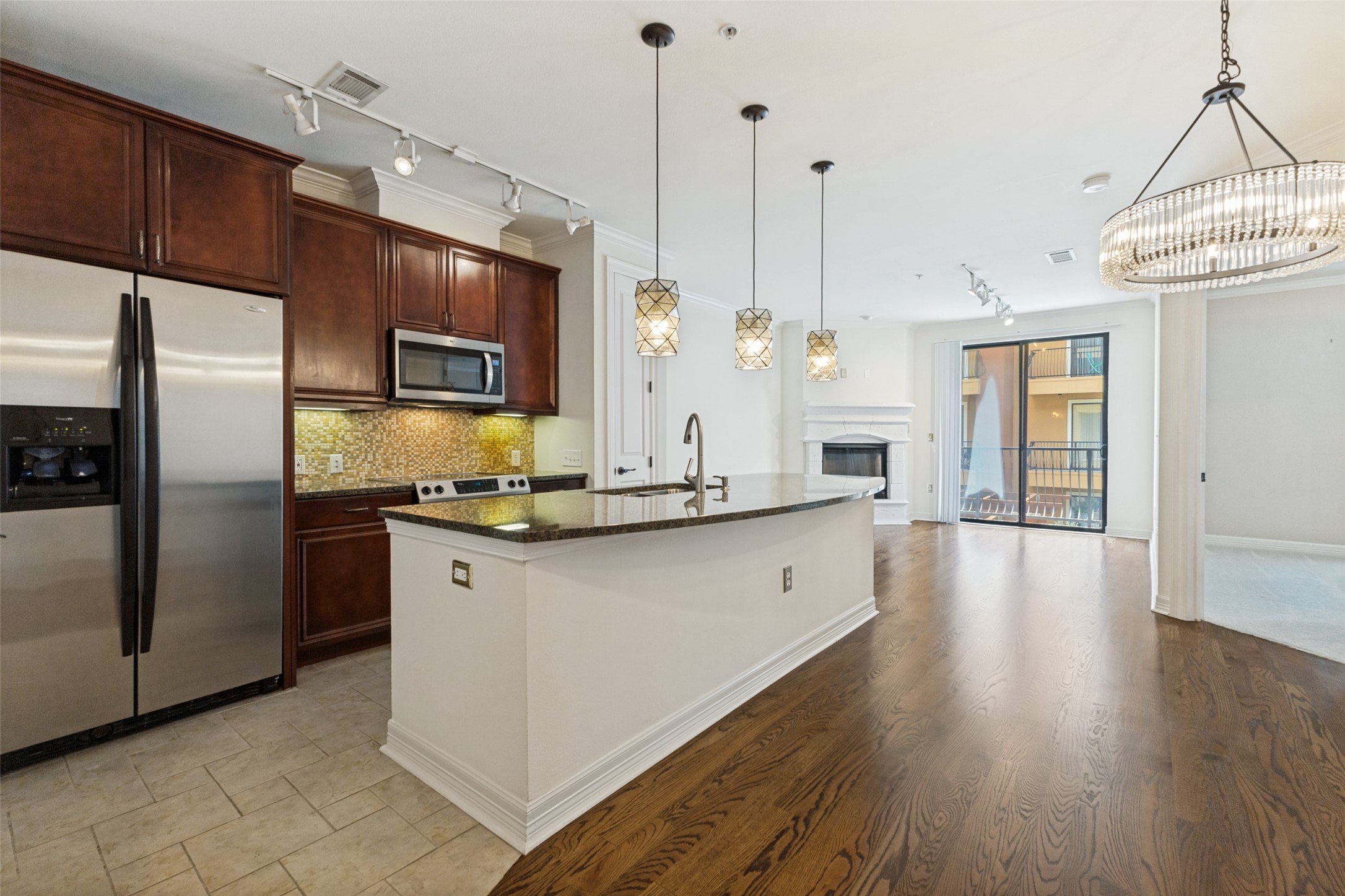 Open-plan condo kitchen with cherry cabinets and granite island opening to a living area with balcony doors.