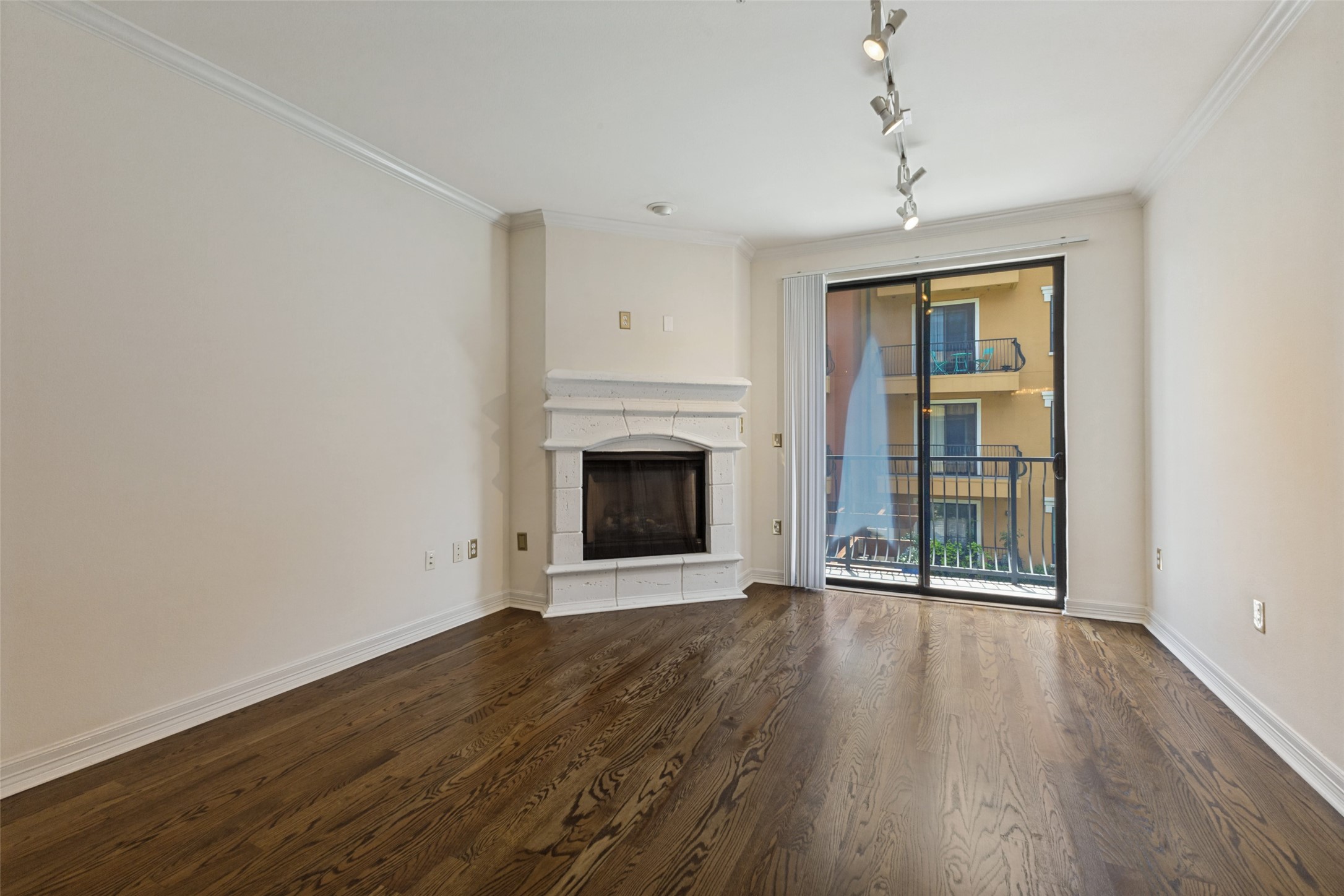 Empty living room with a white corner fireplace, dark hardwood floors, and sliding glass doors to a balcony.