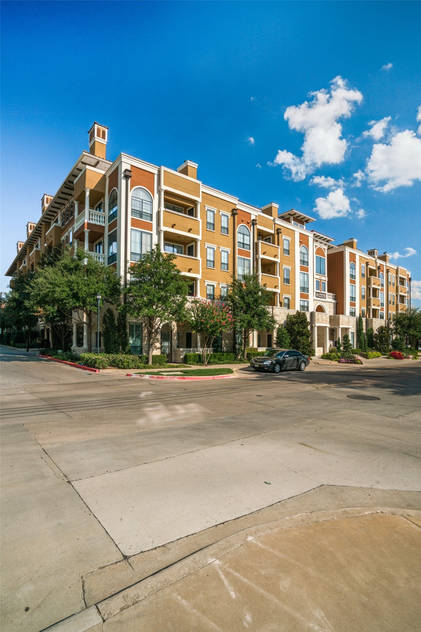 Multistory apartment building with arched windows, balconies, and landscaped grounds.