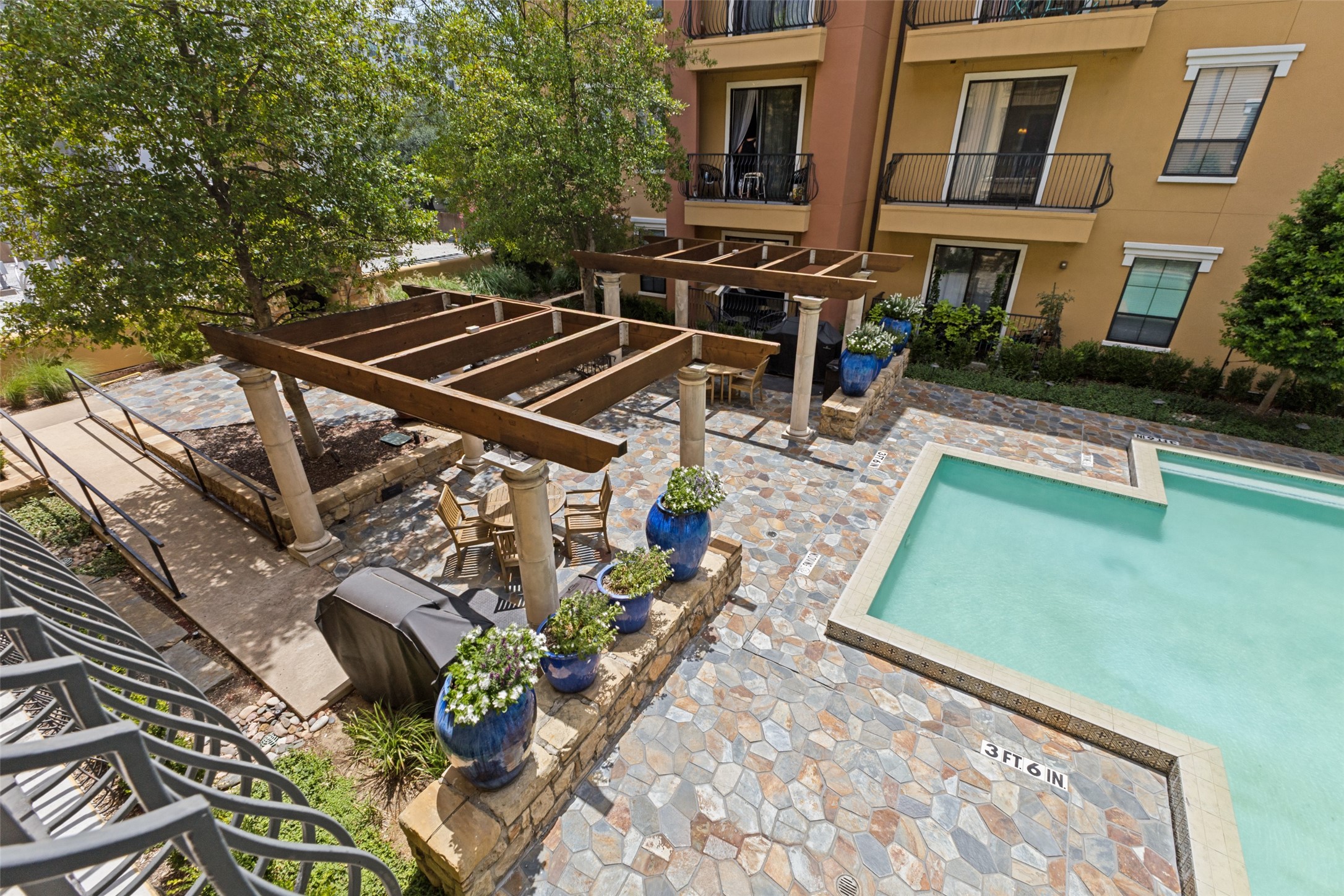 Courtyard swimming pool beside stone-paved deck, wooden pergolas, and blue flower planters.
