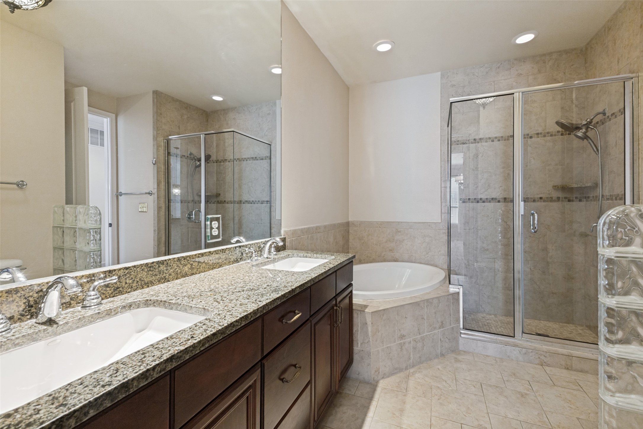 Bathroom with a granite double vanity, corner soaking tub, and glass-enclosed tiled shower.