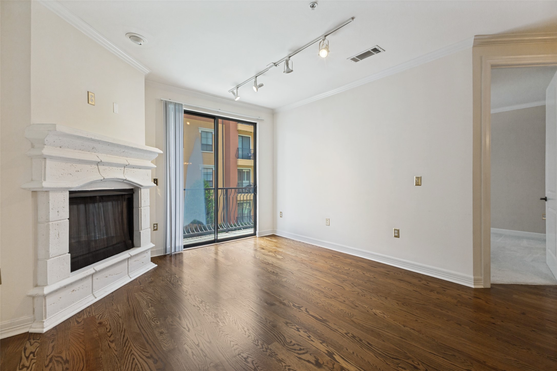 Empty living room with hardwood floors, a white stone fireplace, and sliding glass doors to a balcony.
